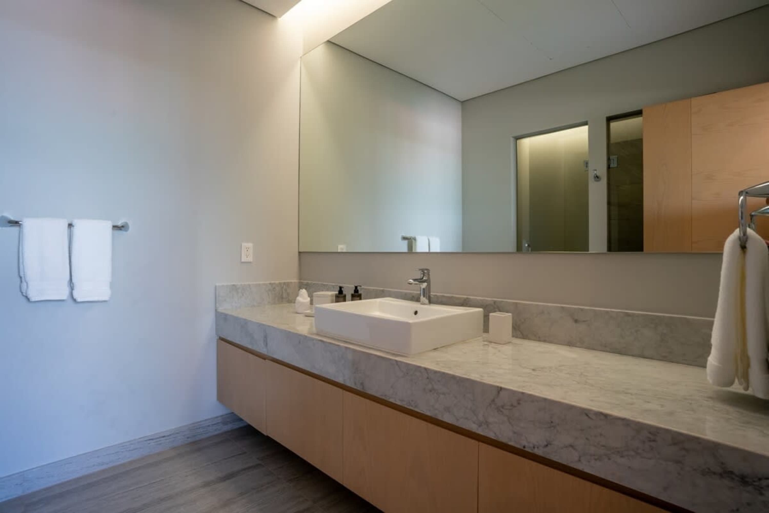 A modern bathroom with a white sink, marble countertop, and light wood cabinets.