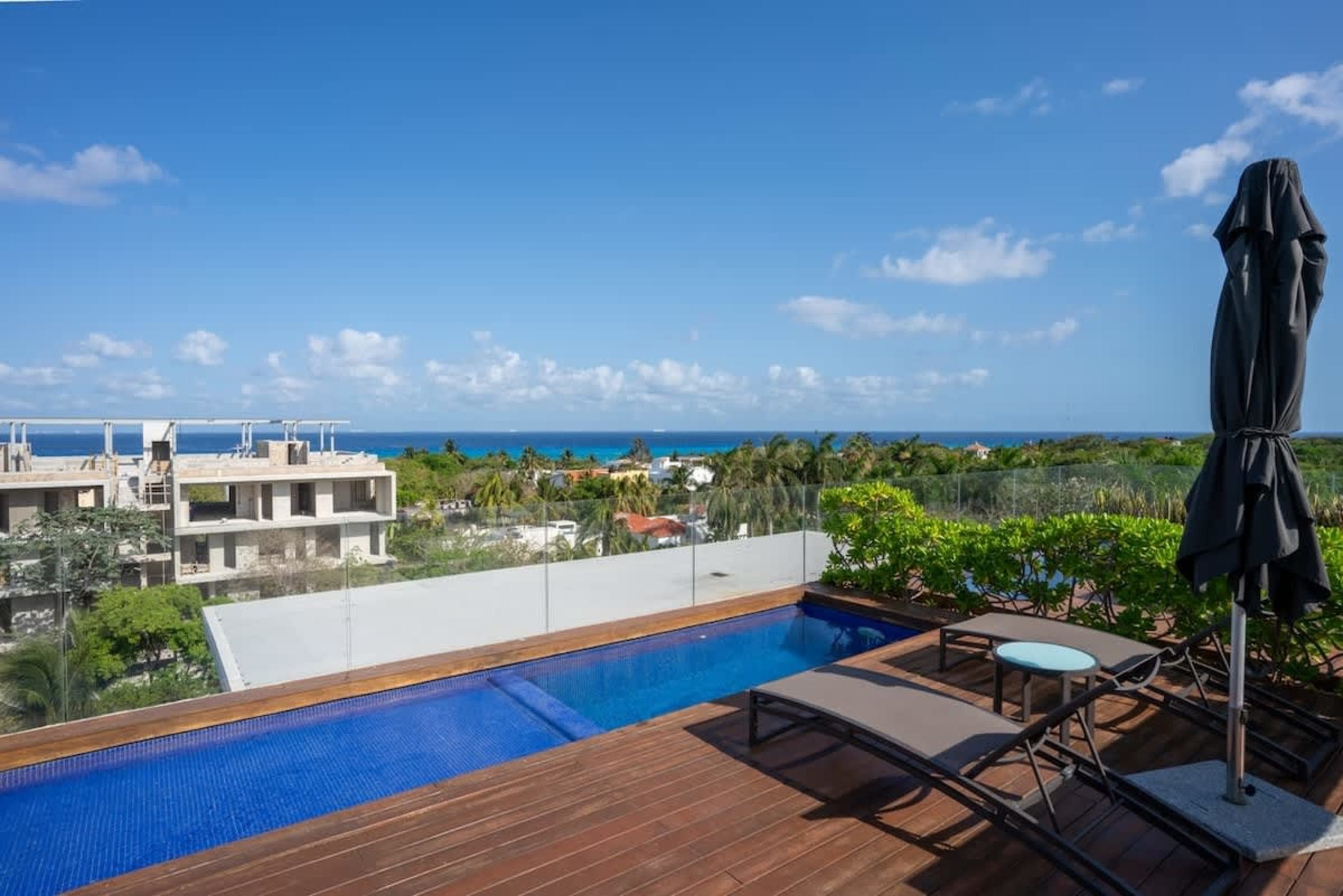 A rooftop pool overlooks the ocean, with lounge chairs and an umbrella.