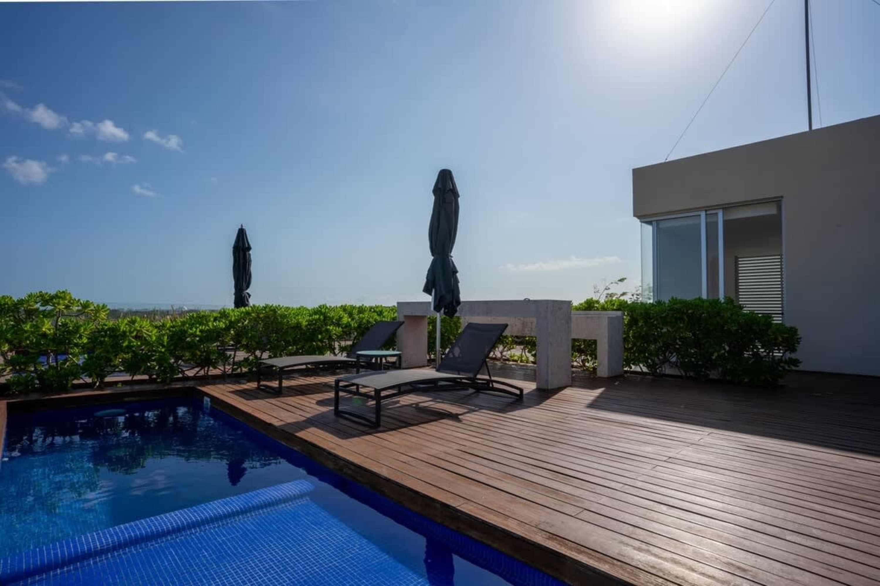 A rooftop pool area with lounge chairs, umbrellas, and a modern building.