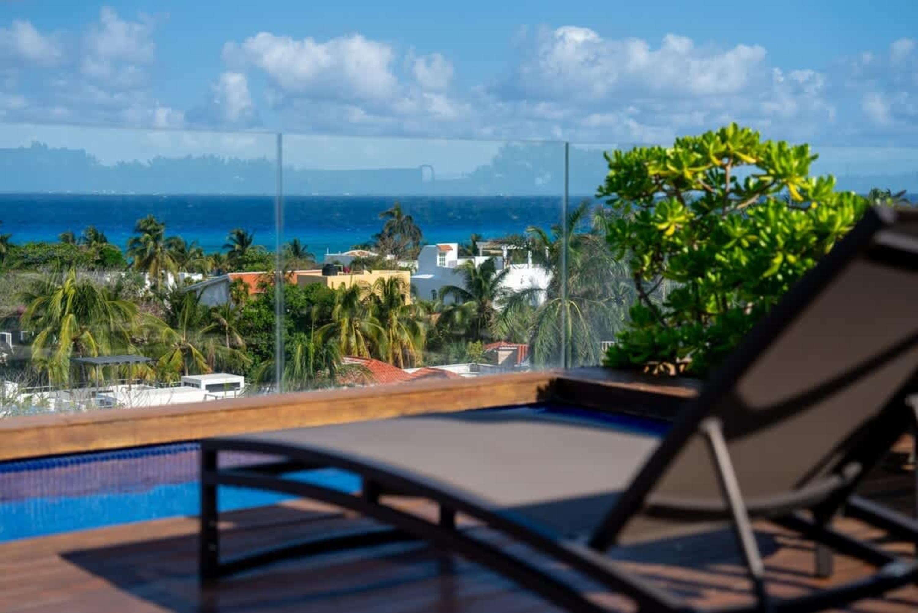 Lounge chair and pool overlook a tropical coastline with palm trees and the ocean.
