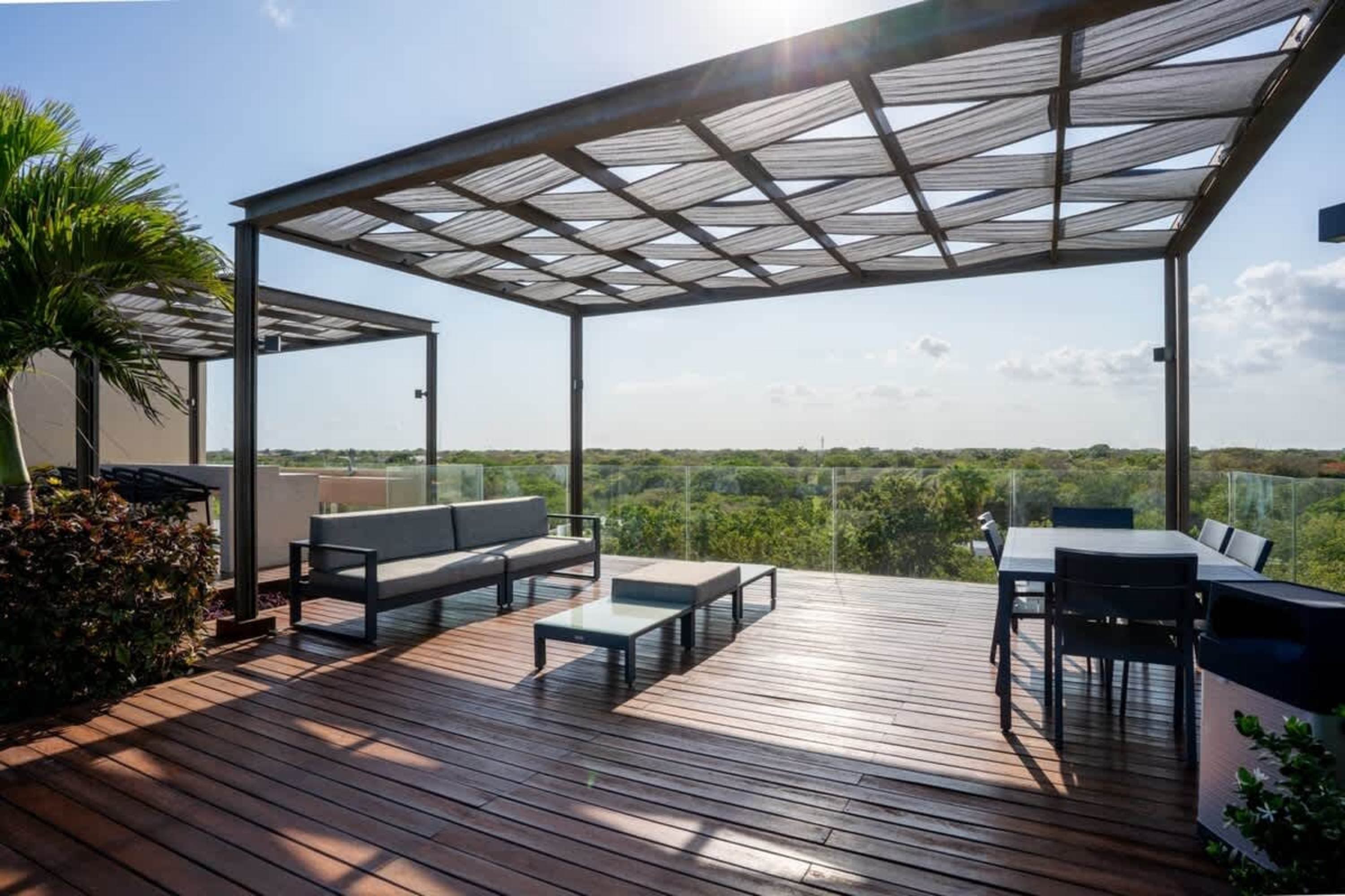 Outdoor terrace with pergola, seating area and dining table overlooking a lush green landscape.