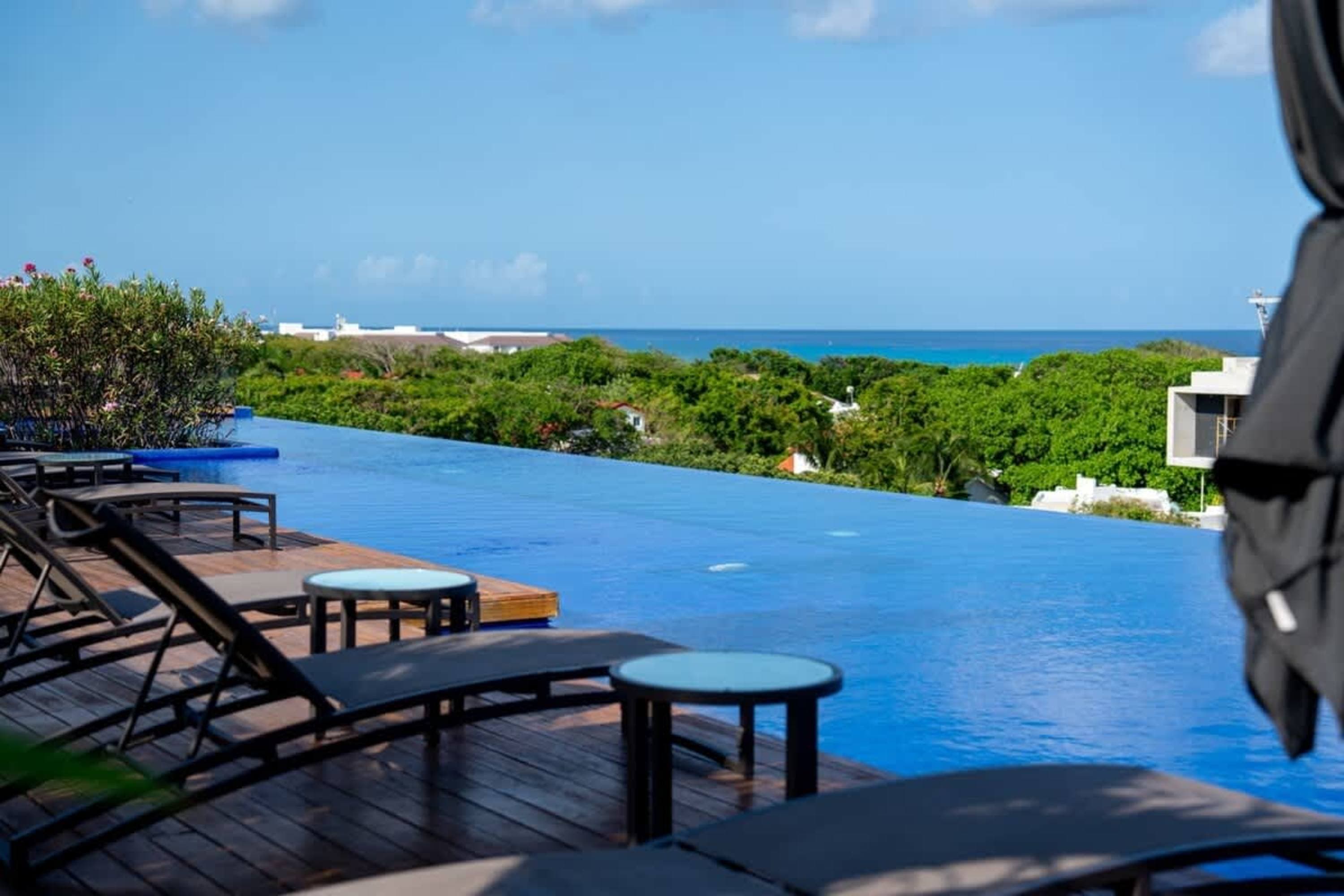Infinity pool overlooking the ocean with lounge chairs and lush greenery.