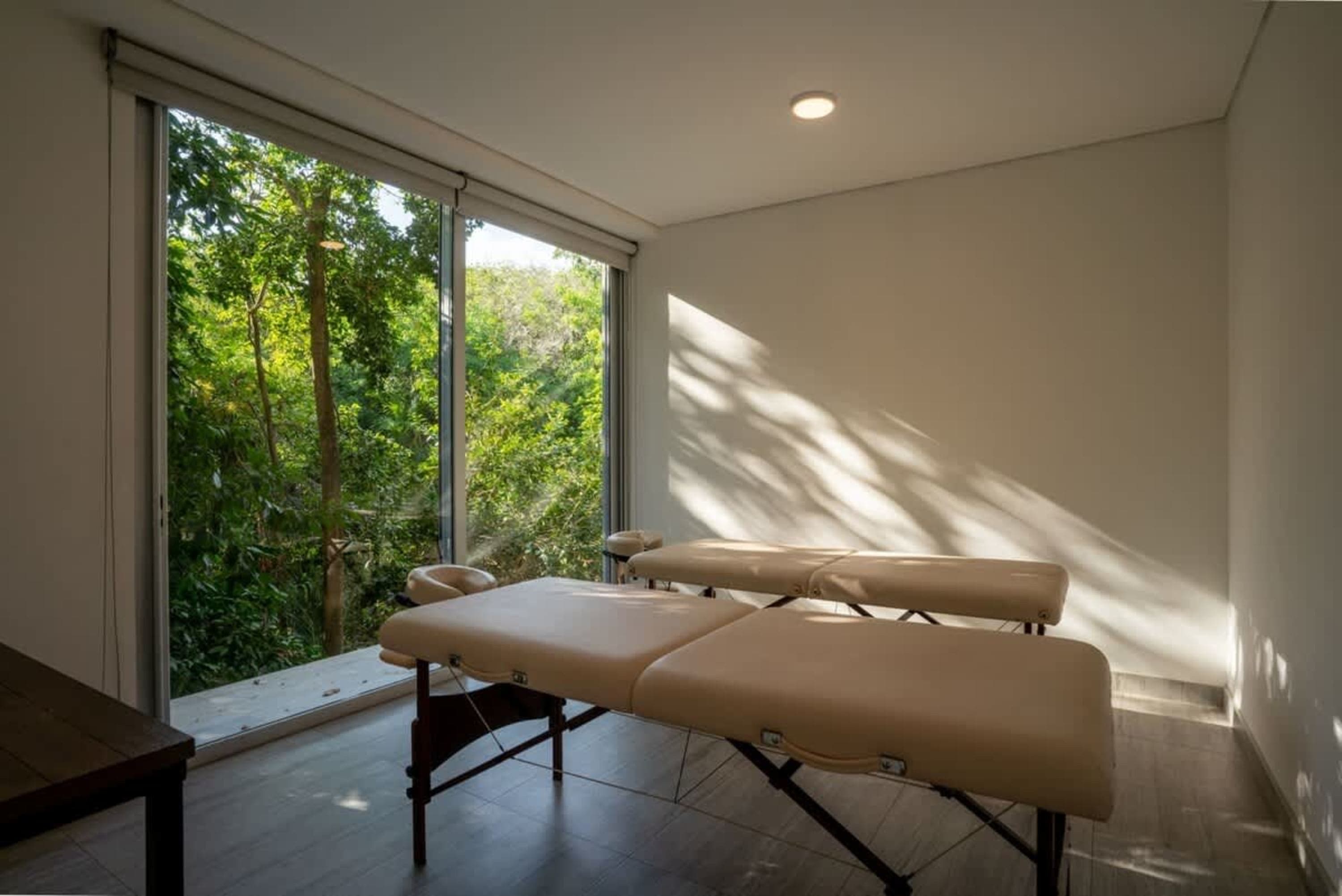 Two massage tables are set up in a room with a large window overlooking trees.