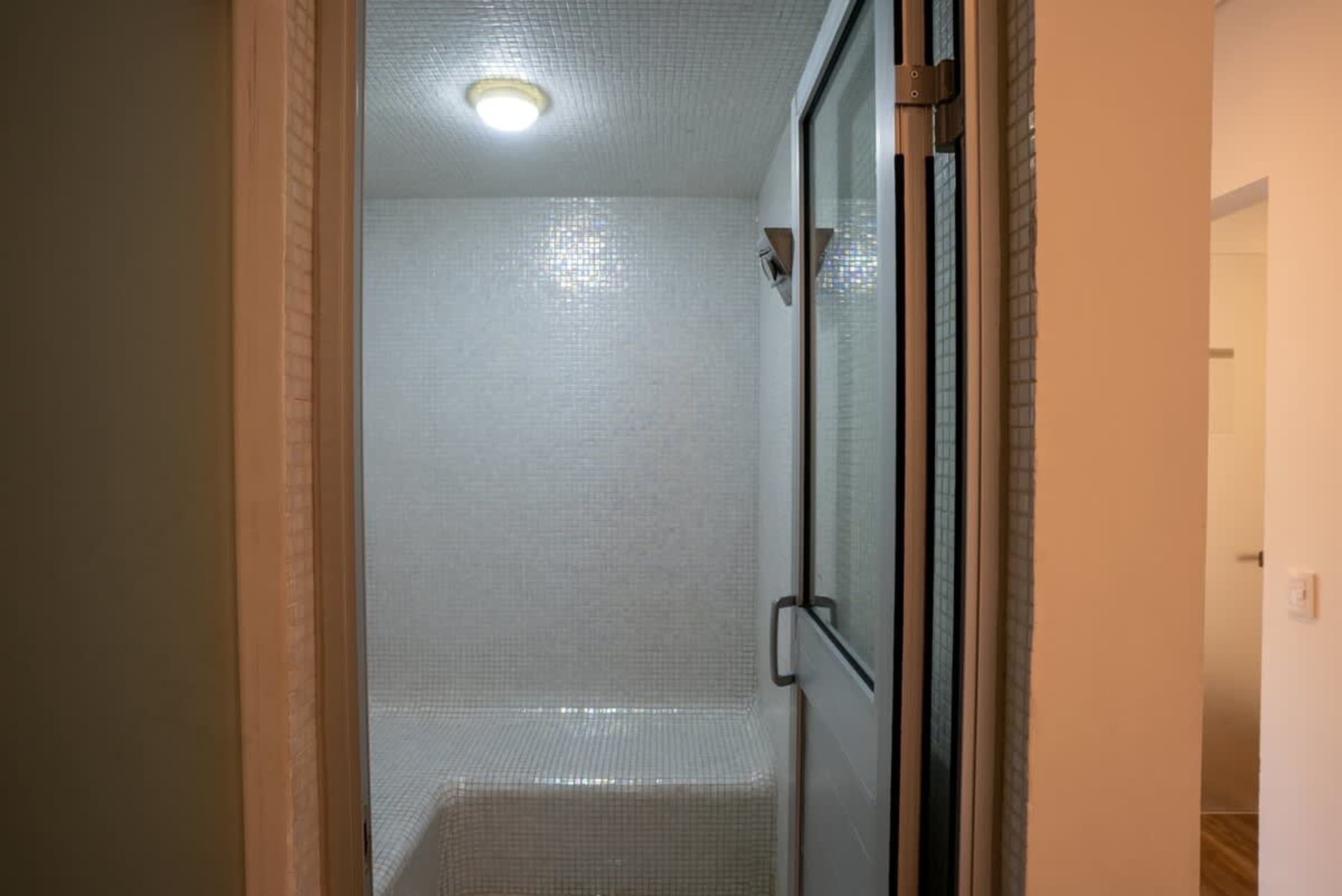 A white tiled steam room with a glass door.