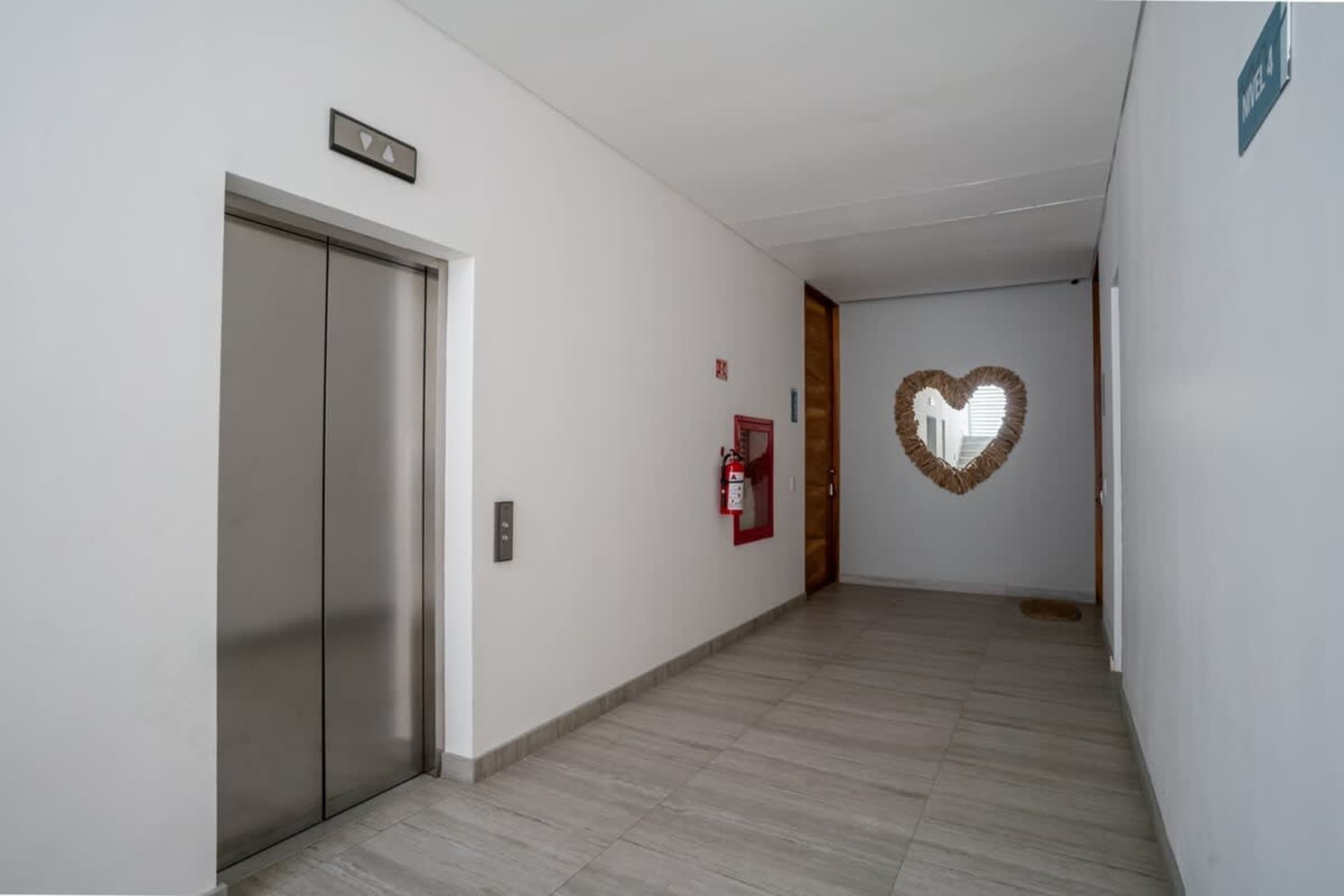 An elevator with a heart-shaped mirror and a fire extinguisher on a white wall.