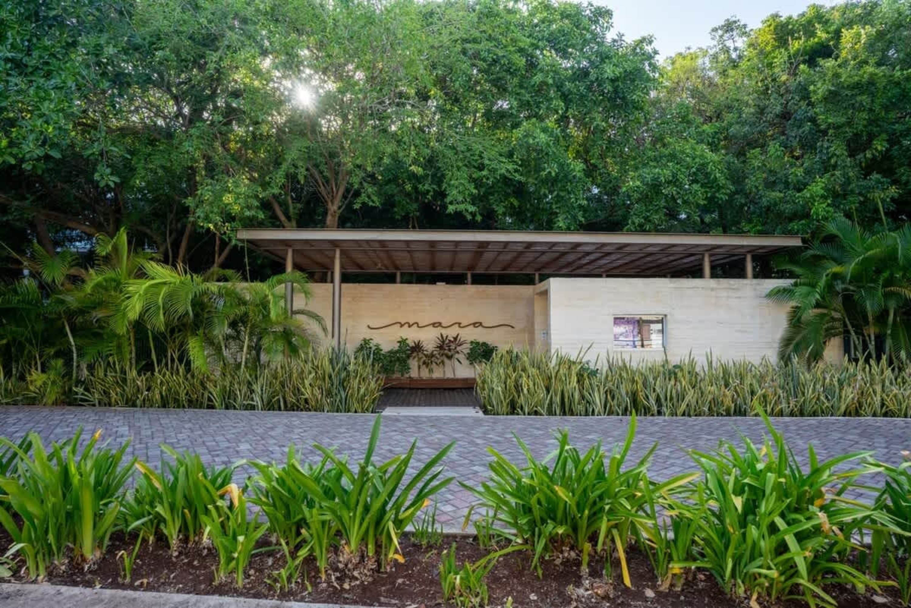 A building entrance with "mara" signage, surrounded by lush greenery and trees.