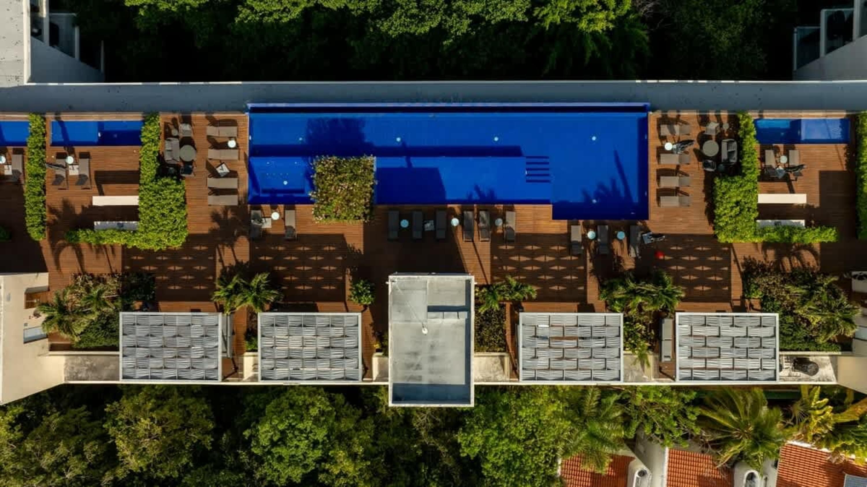 Aerial view of a modern rooftop pool with lounge chairs, wooden deck, and lush greenery.