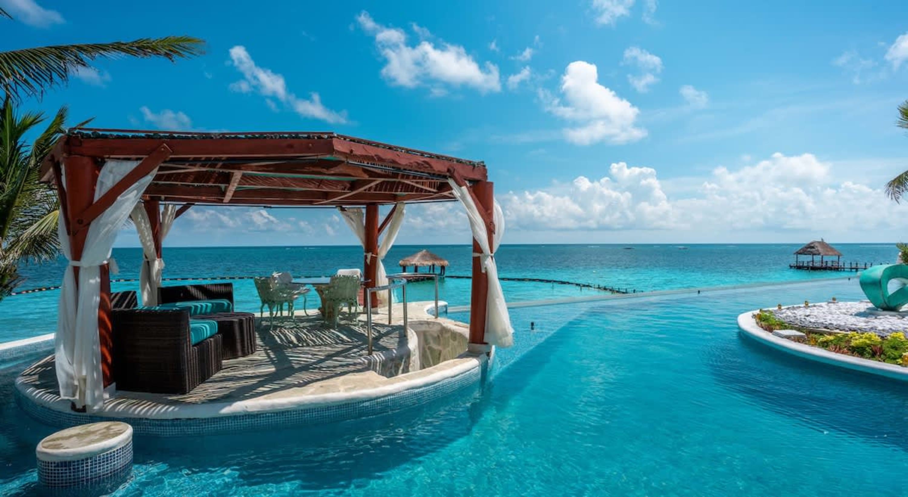 A luxurious infinity pool overlooks the ocean, with a covered seating area and palm trees.