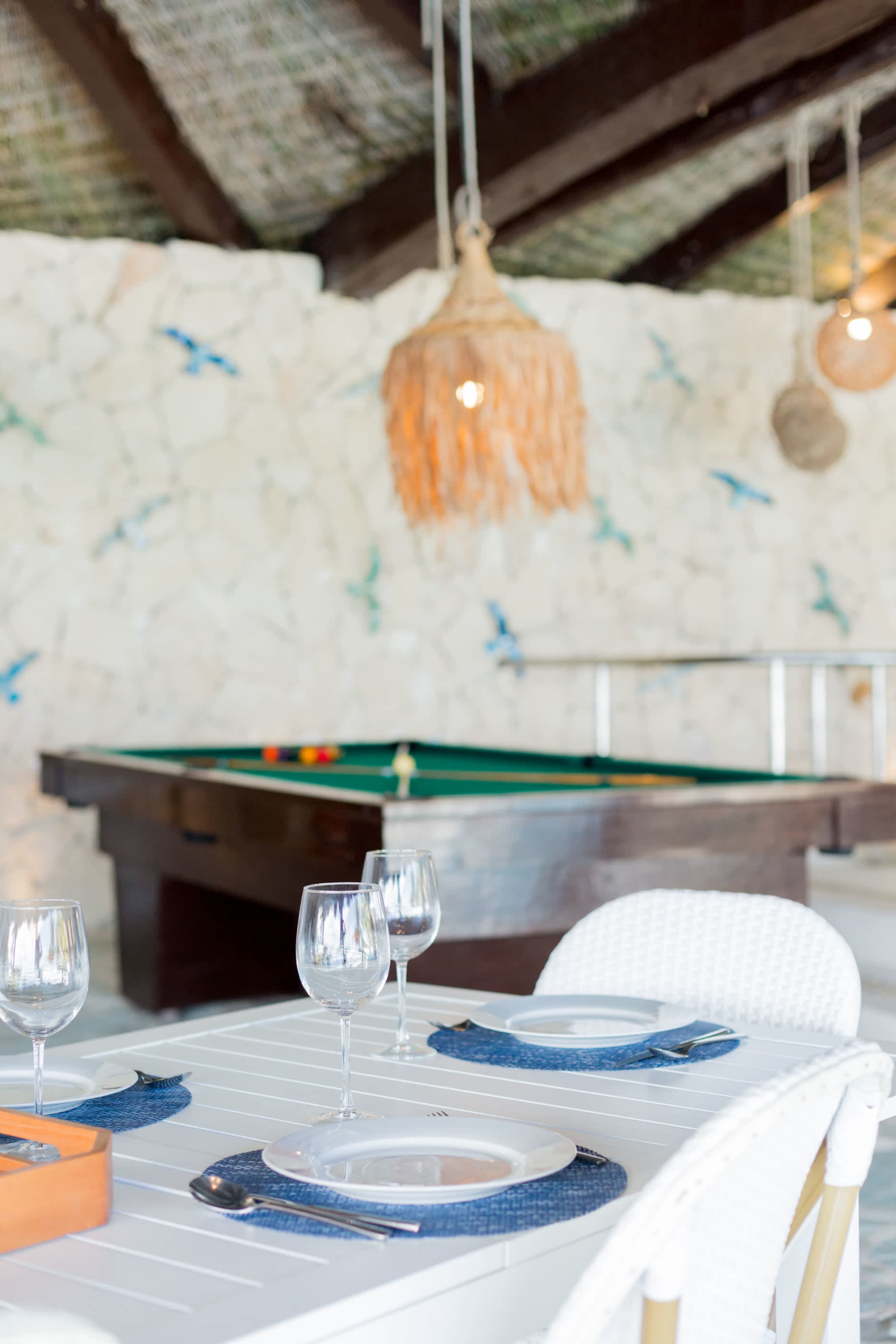 Dining table set with plates and wine glasses in front of a pool table.
