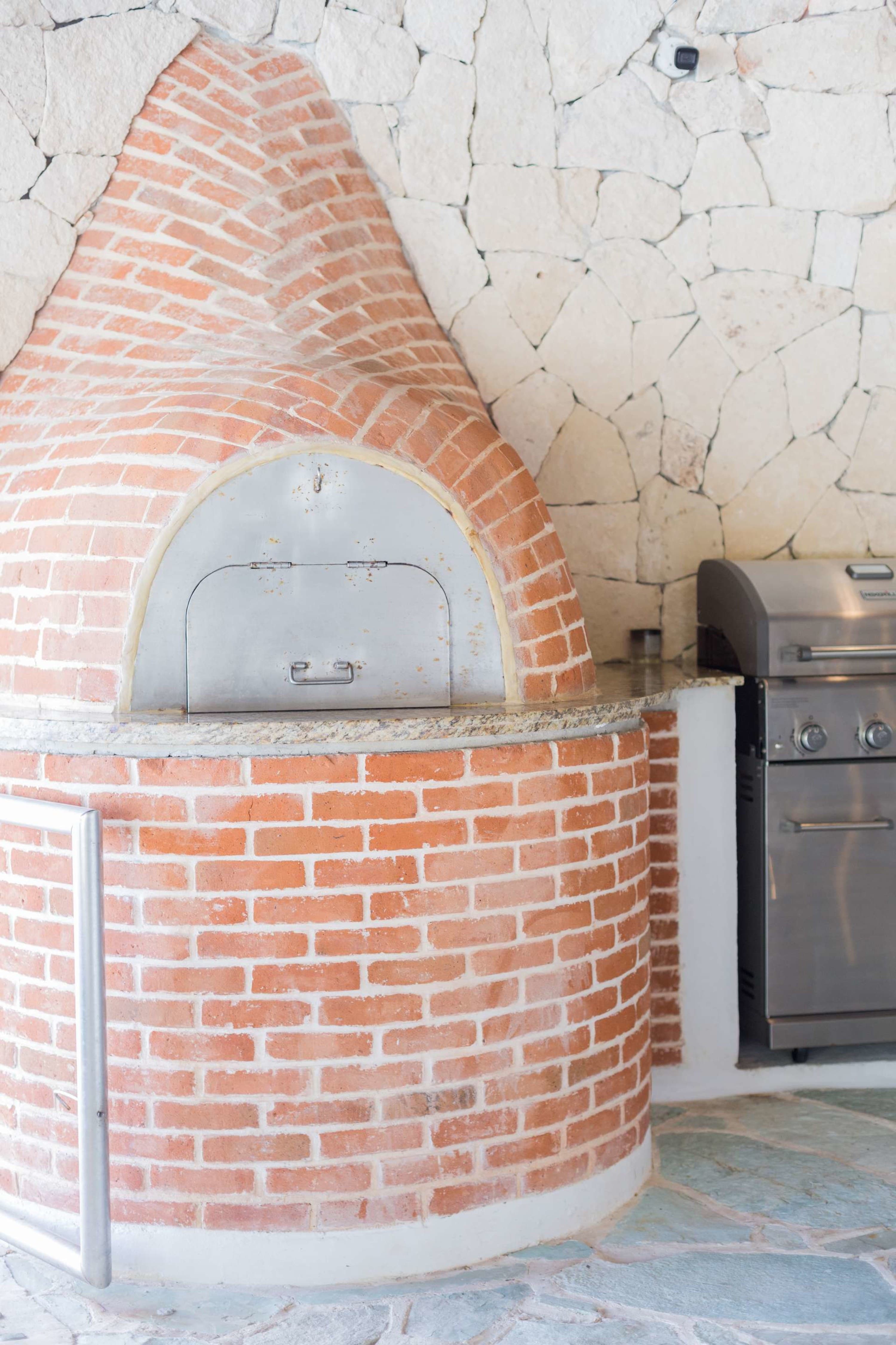 Outdoor brick pizza oven with a stainless steel door and a grill next to it.
