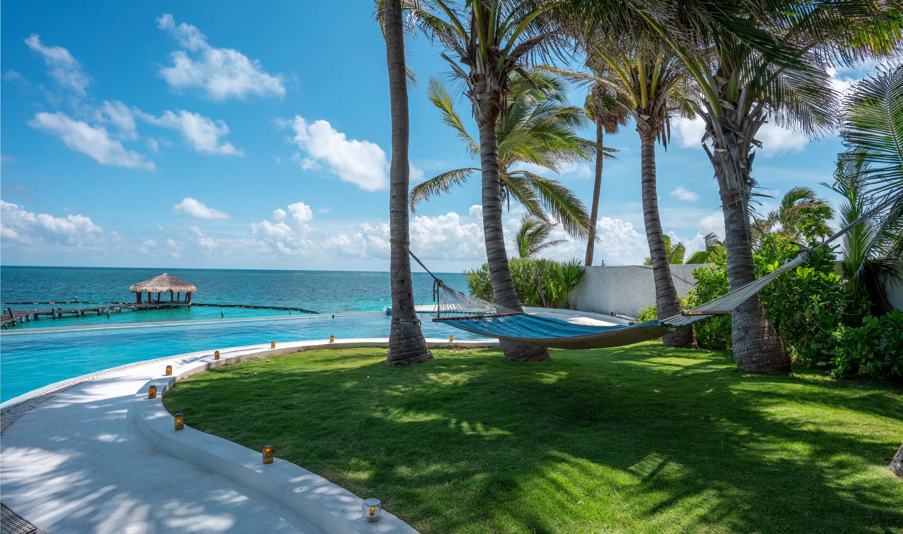 Hammock between palm trees by an infinity pool and the ocean.