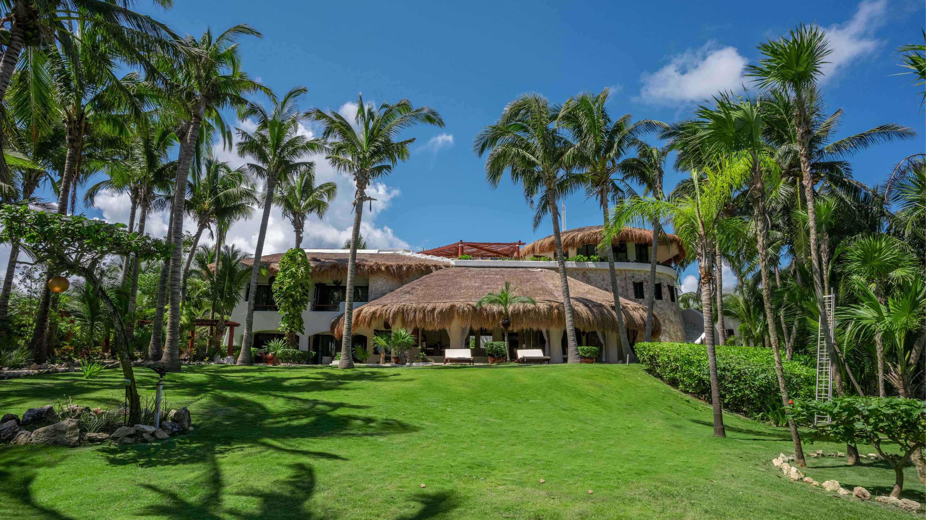 A luxury tropical villa with thatched roofs and palm trees.