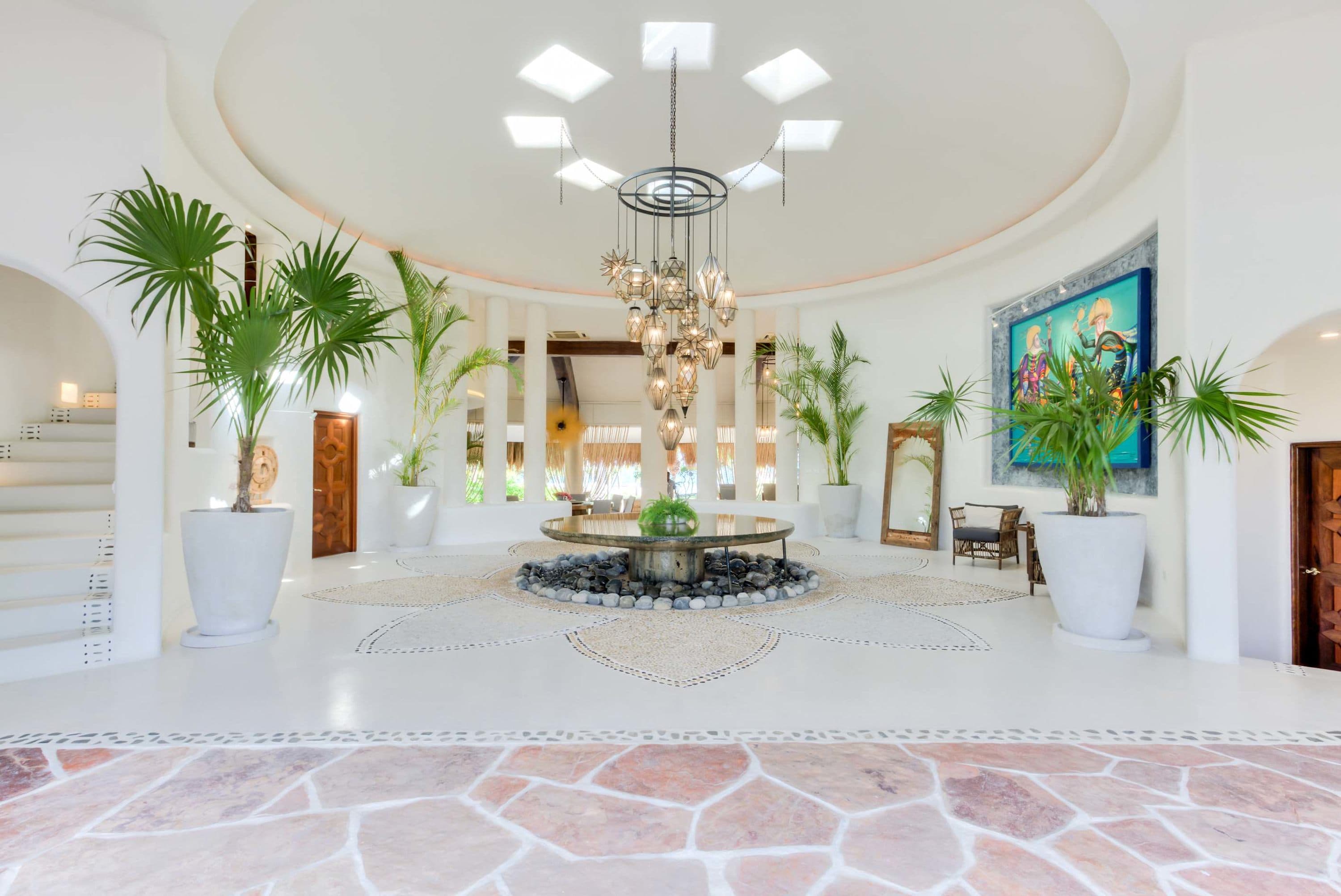 An entryway with a large chandelier, potted plants, and a mosaic floor design.