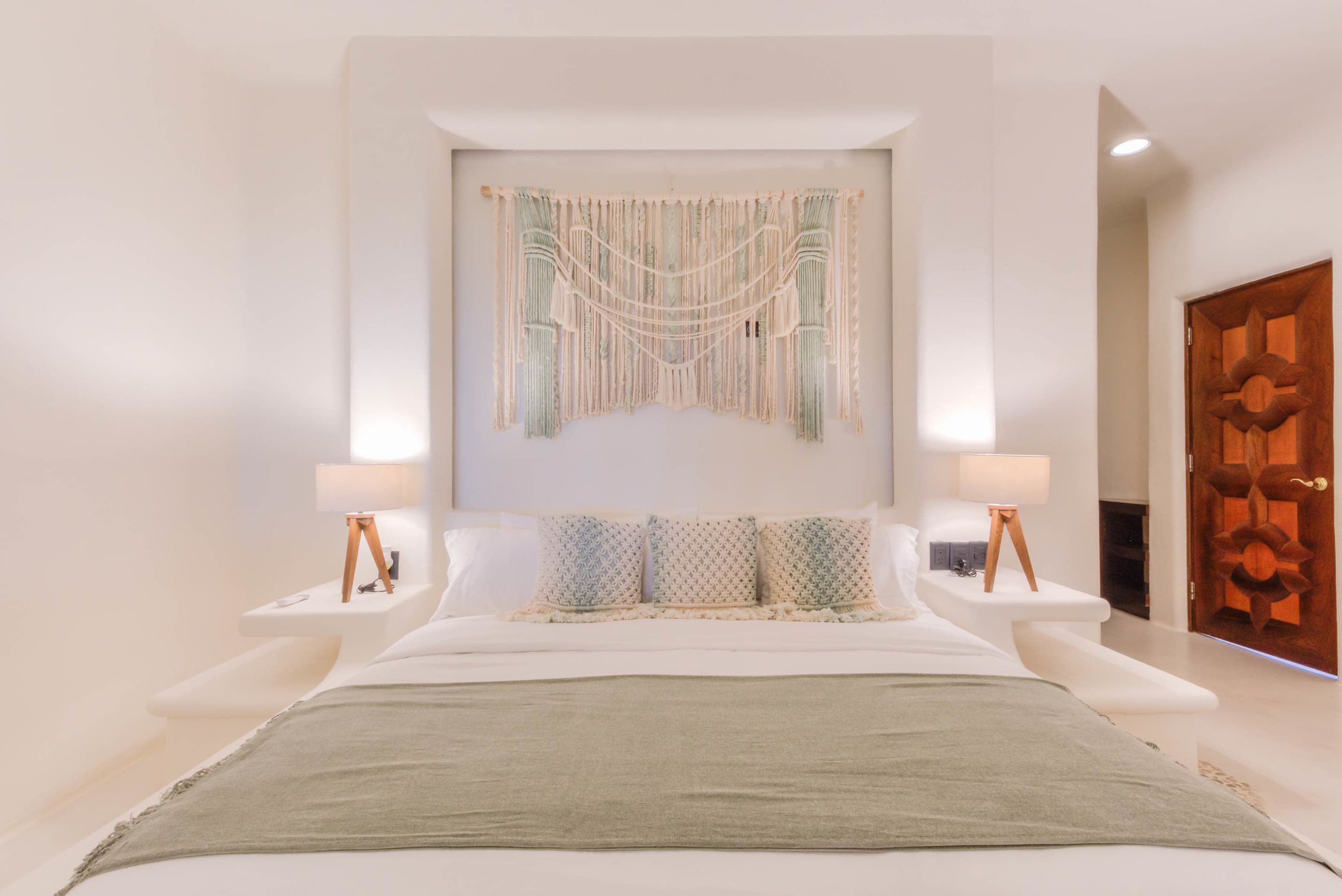 A bed with white bedding, decorative pillows, and a sage green throw blanket.