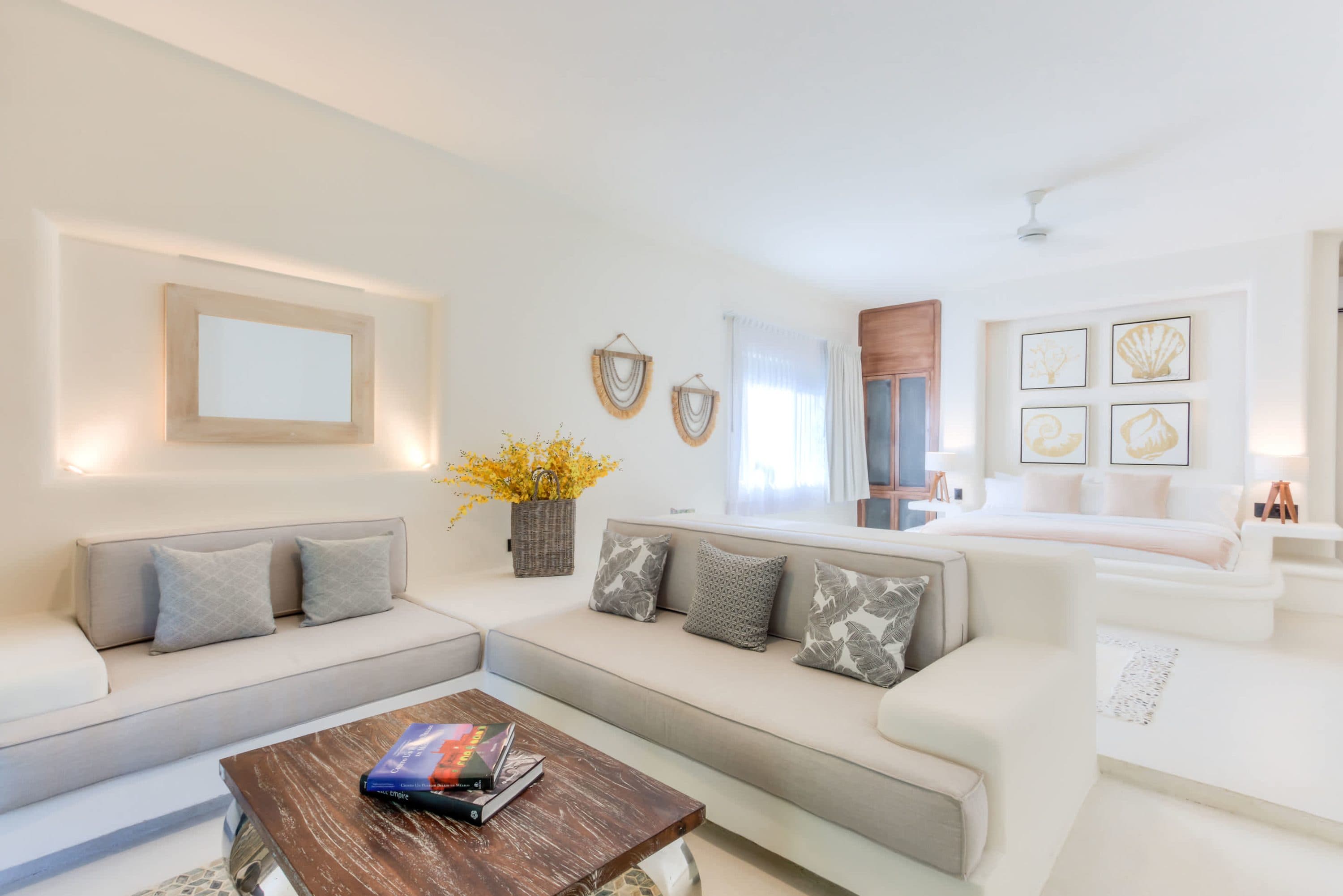 A bright, white living room and bedroom with light gray sofas and a bed.