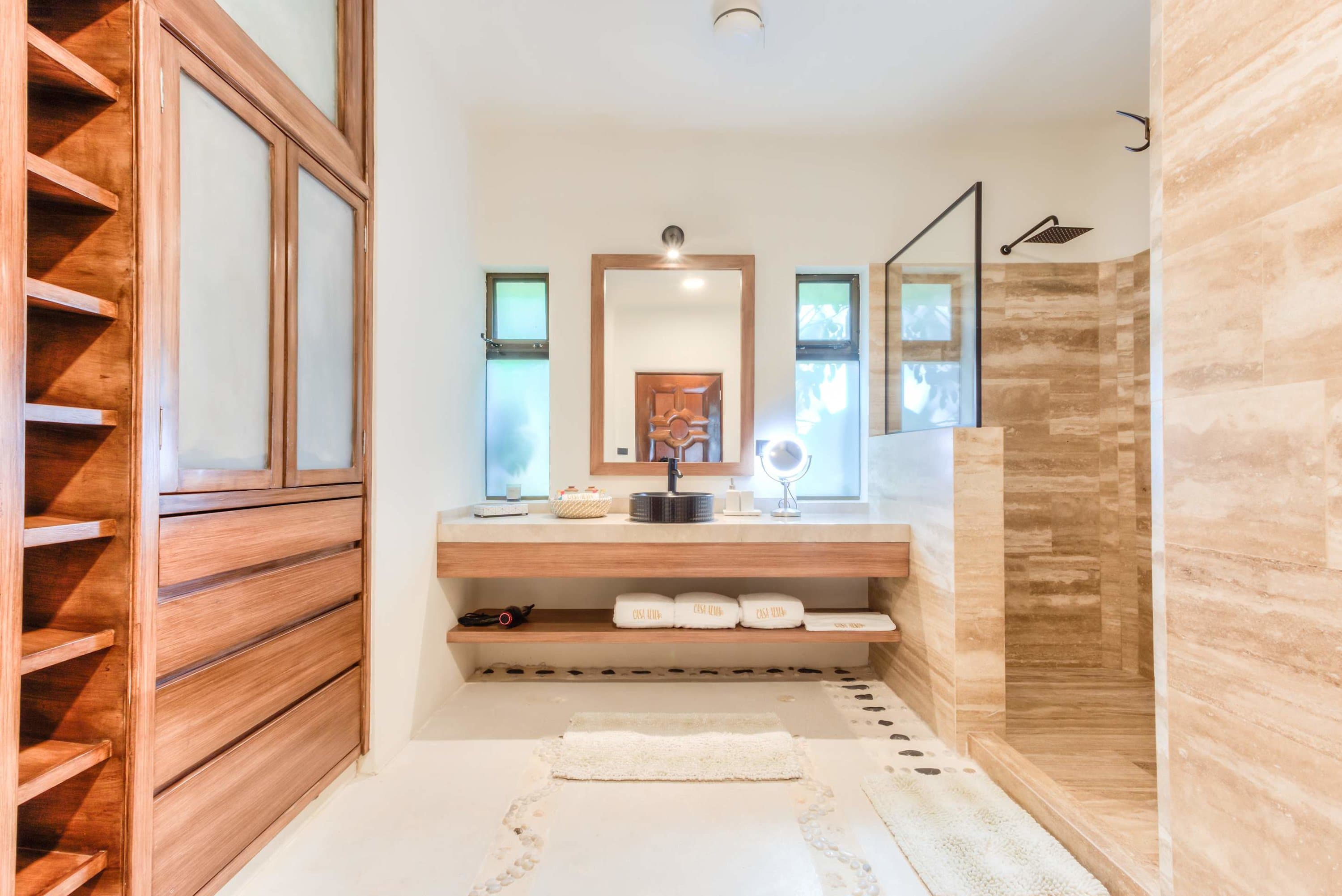 A luxurious bathroom with wooden cabinets, stone tiles, and a glass-enclosed shower.