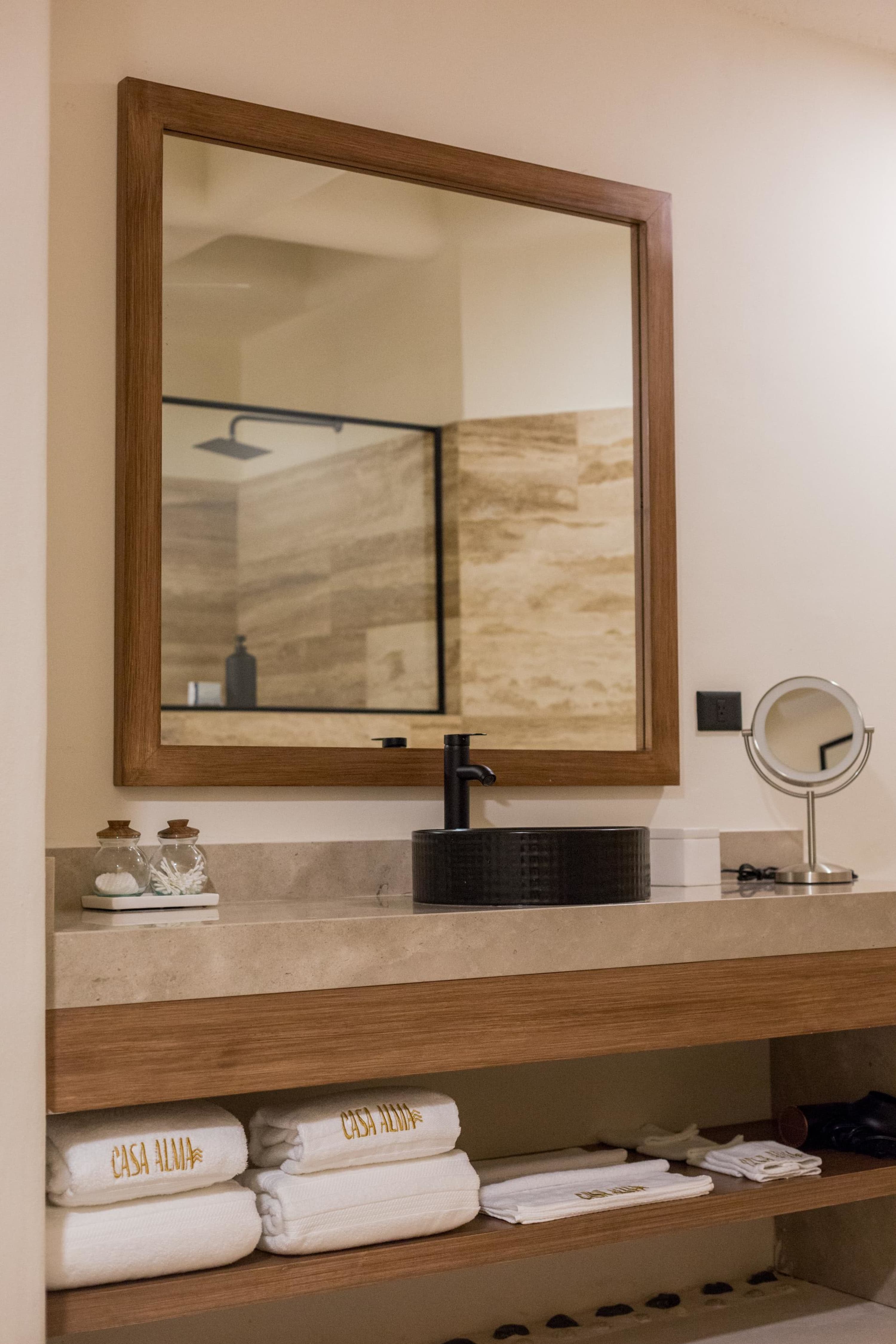 A bathroom vanity with a sink, mirror, and towels on a wooden shelf.
