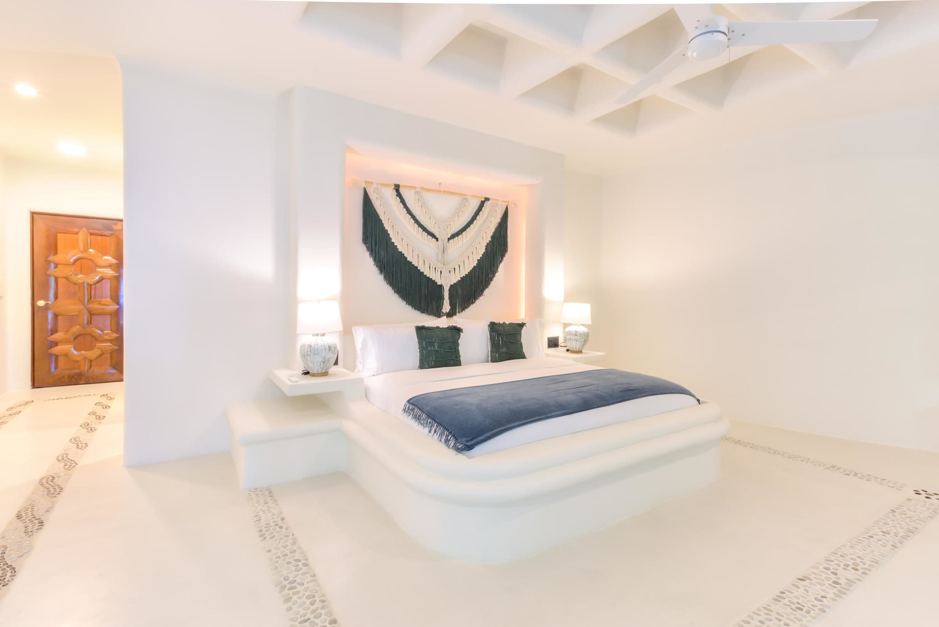 A bedroom with a king-size bed and macrame wall art.