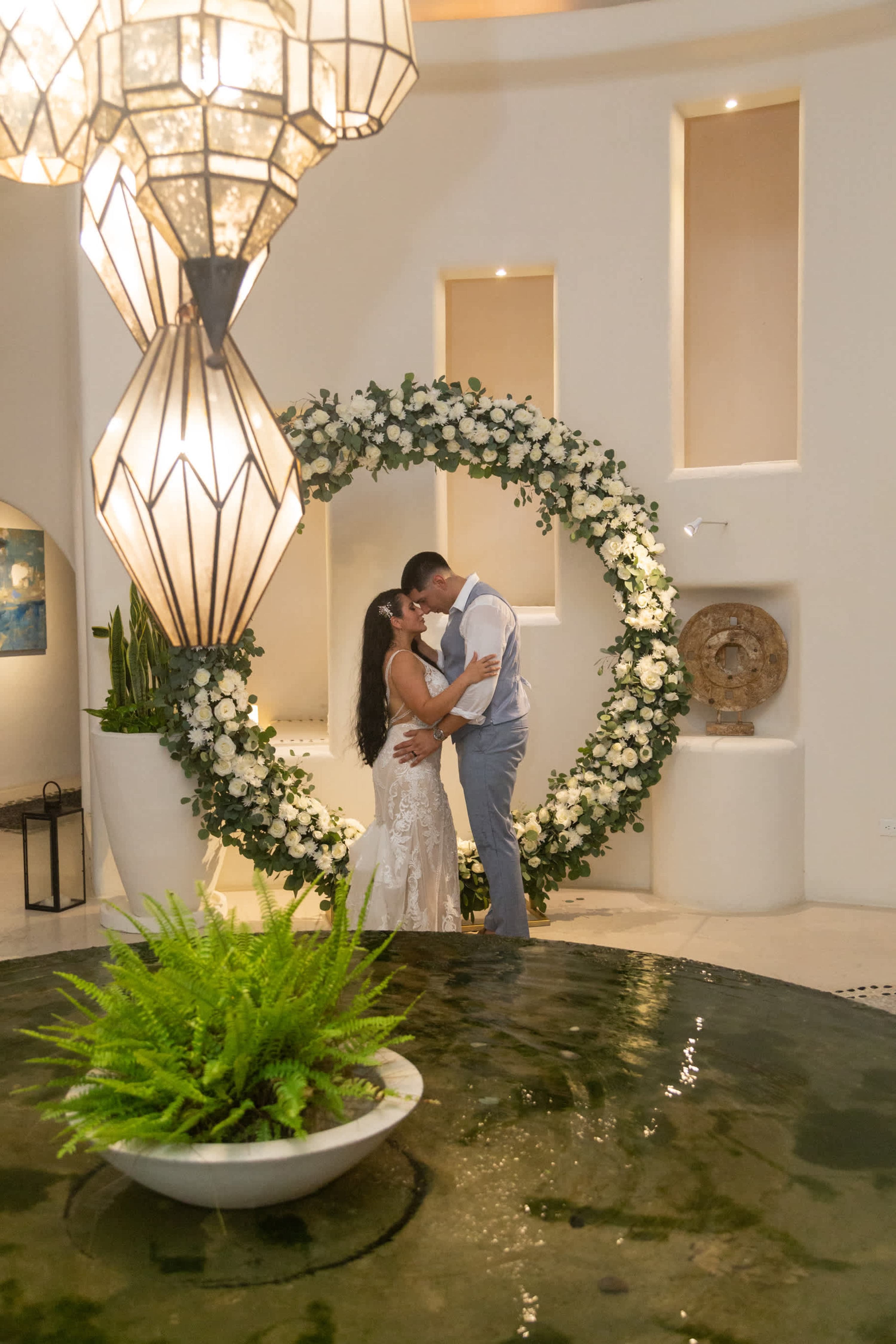 Bride and groom kiss in front of a floral archway.