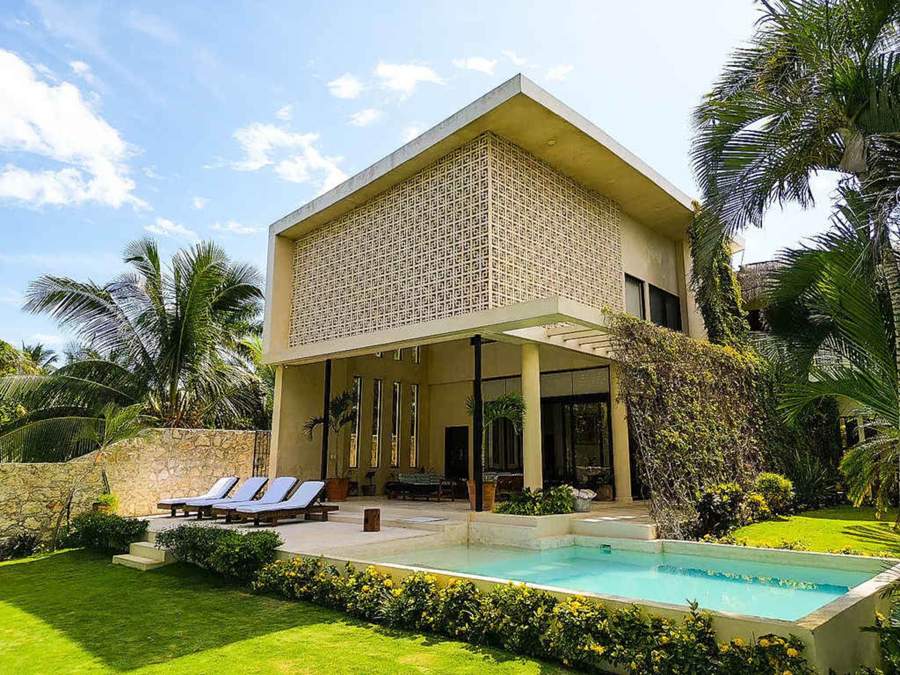 Modern villa with pool and lounge chairs surrounded by lush greenery.