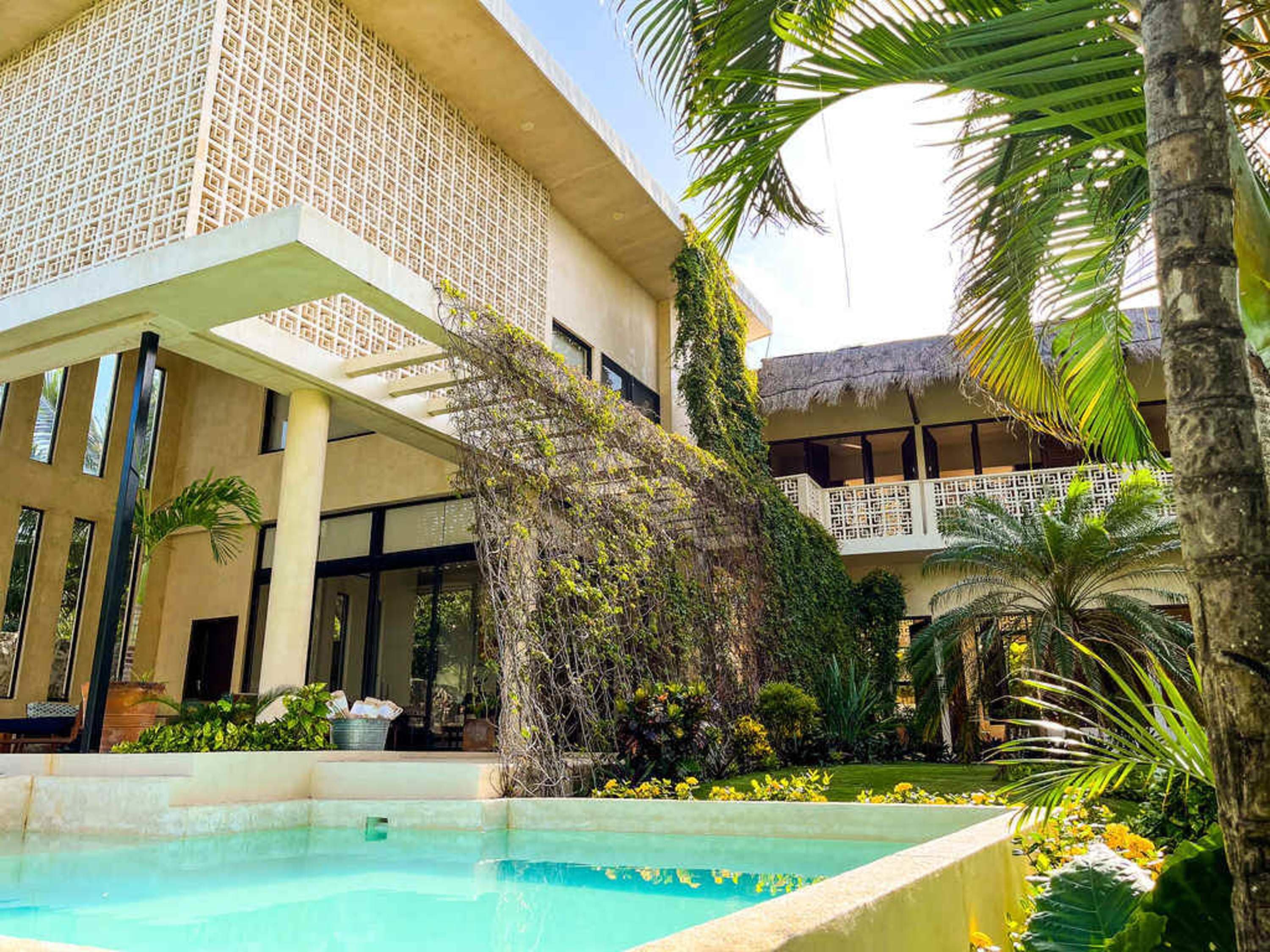 A private swimming pool is in the foreground of a luxury modern home with lush greenery and palm tre