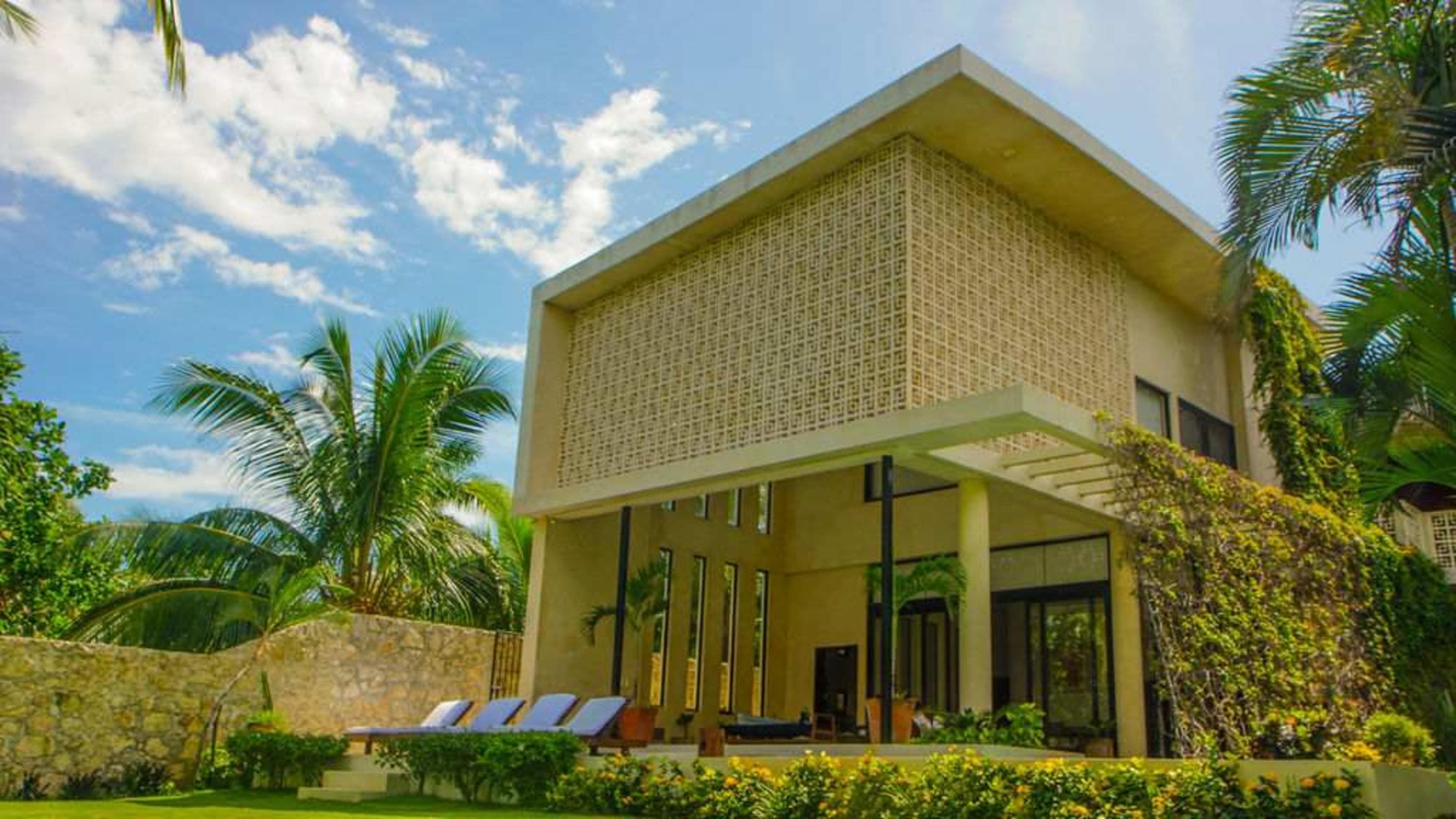 Modern house with geometric facade, palm trees, and lounge chairs.