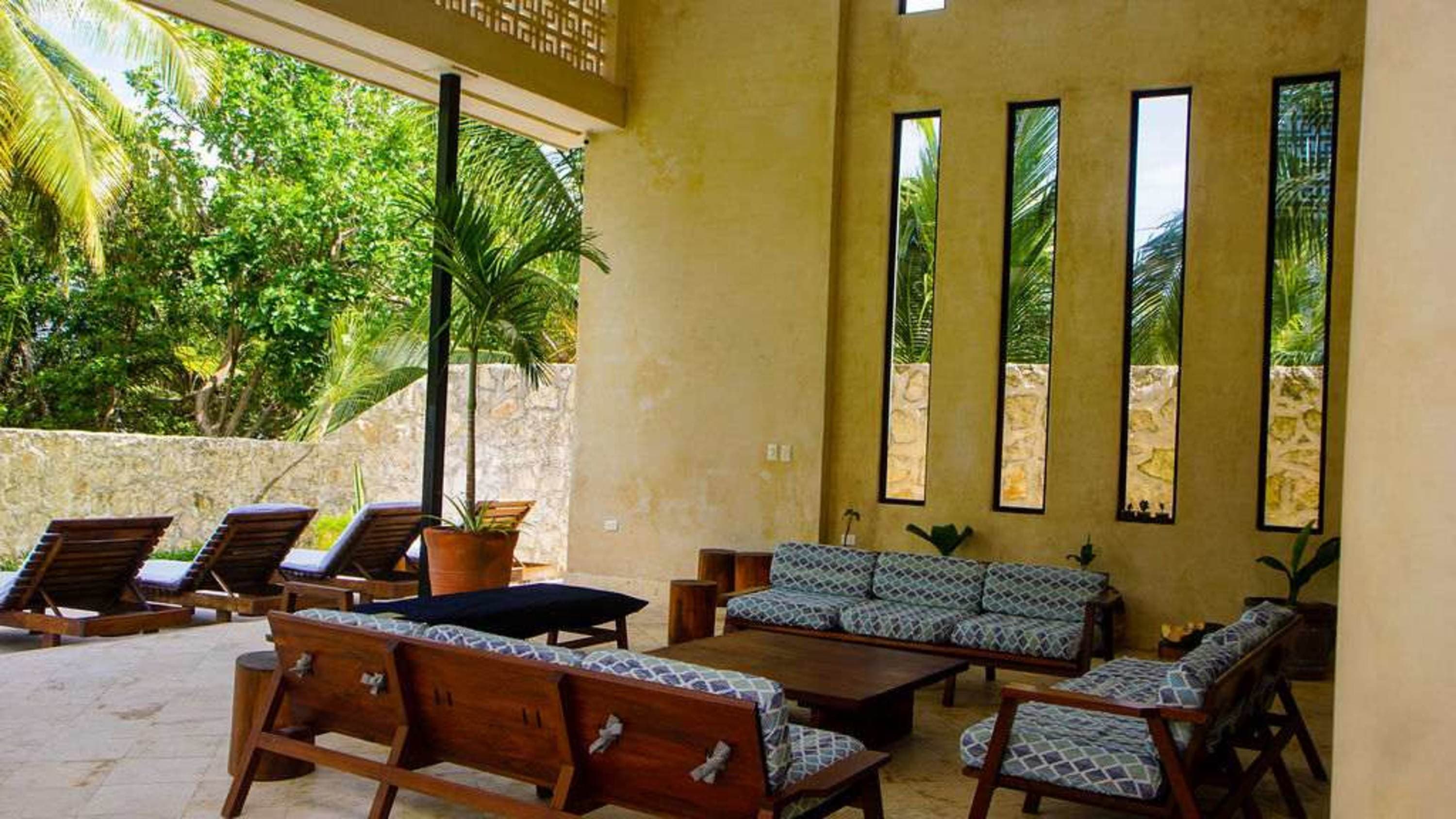 An outdoor living area with lounge chairs and sofas, surrounded by lush greenery.