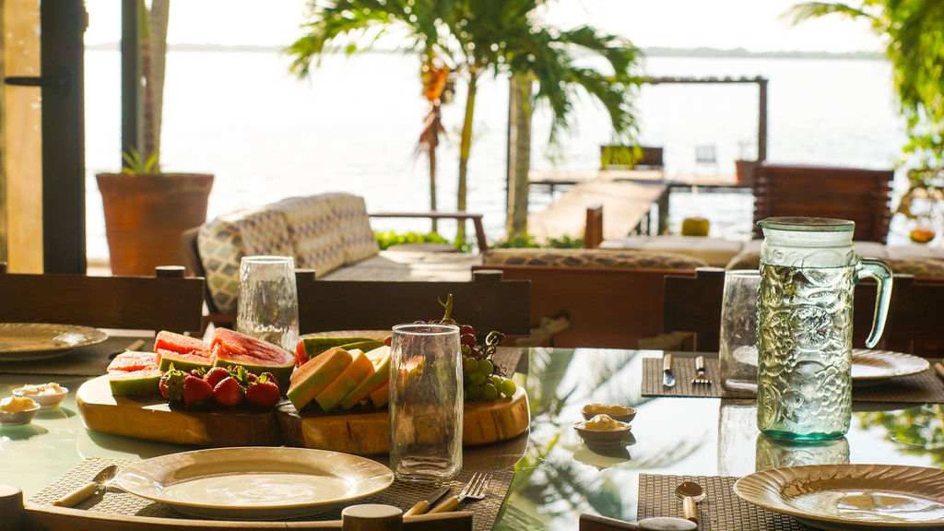 A table set for breakfast outdoors with fruit, plates, and a pitcher of water.