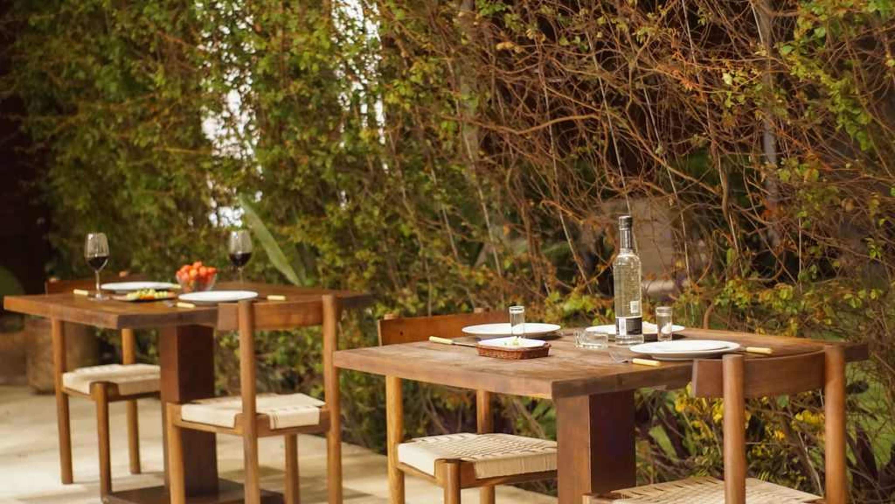 Outdoor dining setting with wooden tables and chairs, set with plates, glasses, and a bottle of wine