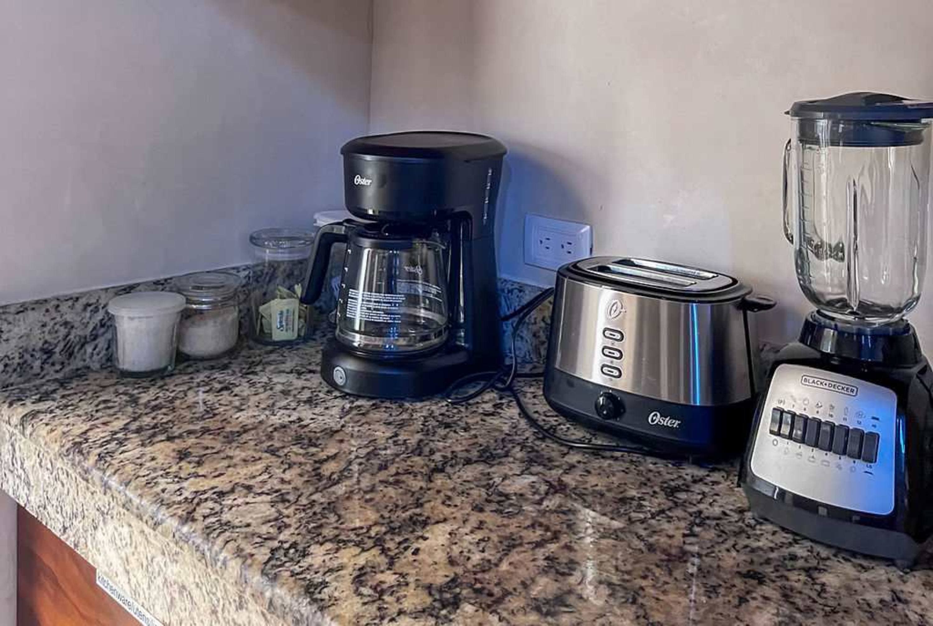 Kitchen counter with blender, toaster, coffee maker, and jars of sugar and sweetener.