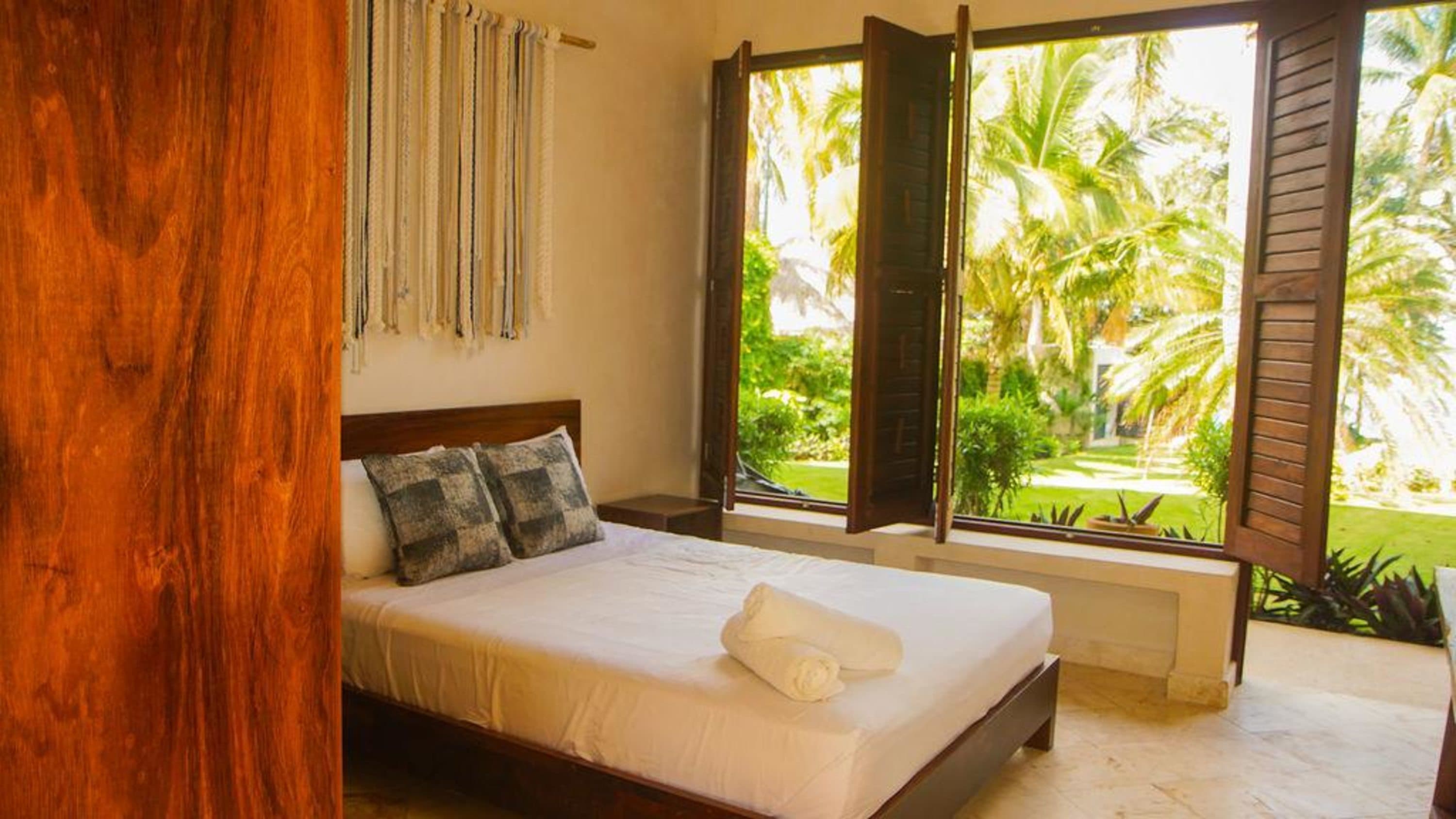 A bedroom with a large window overlooking palm trees.