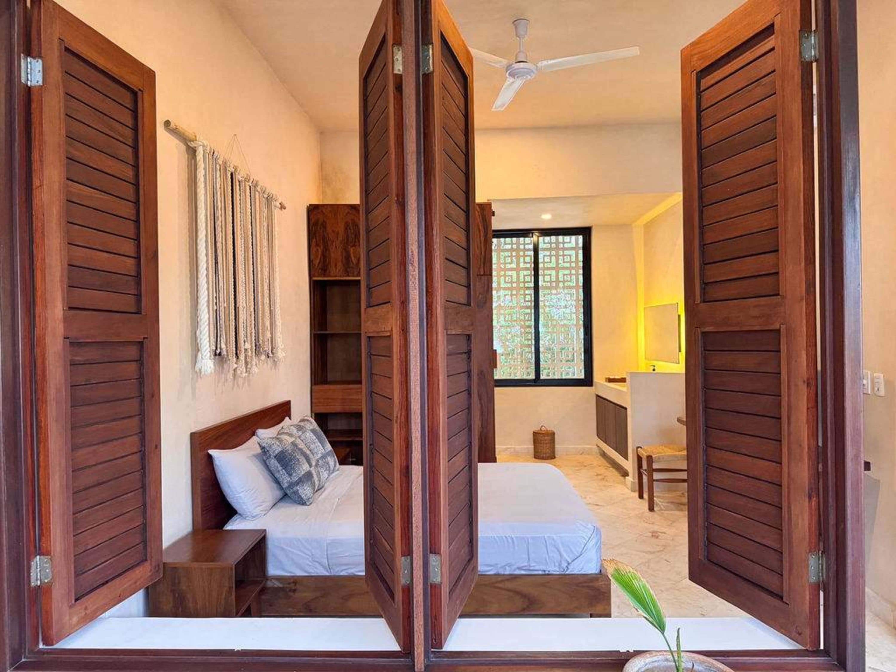 Interior view of a bedroom with open wooden shutters, a bed with white linens, and a ceiling fan.