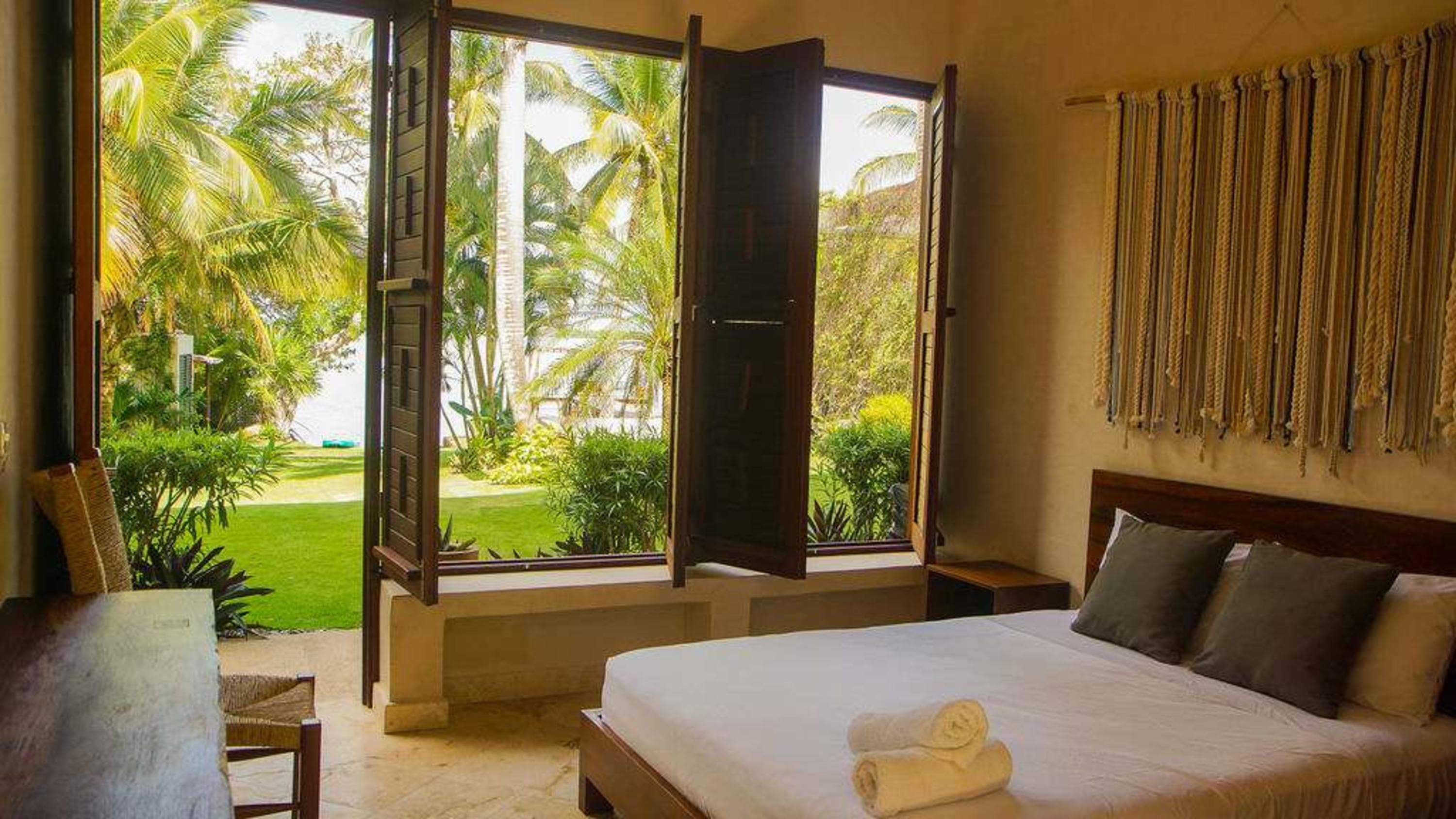 A bedroom with a bed, two pillows, a bedside table, and open windows.