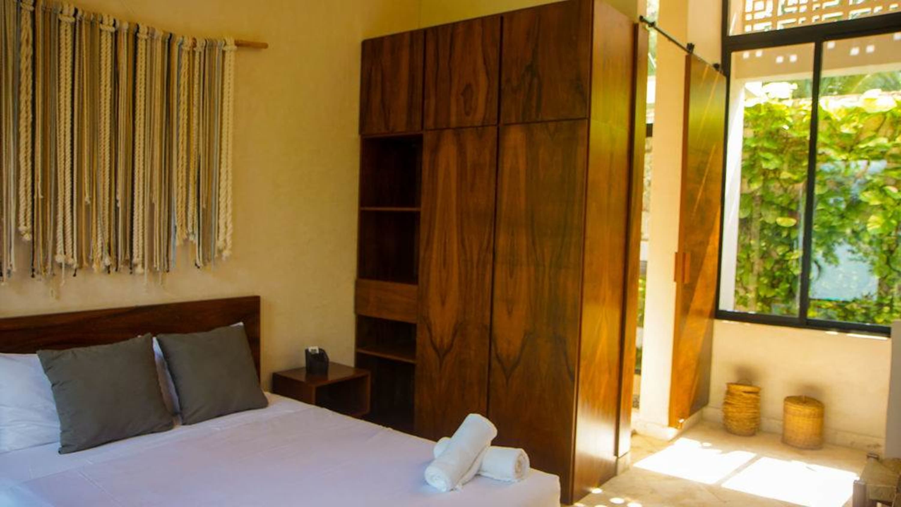 A bedroom with a macrame wall hanging and wooden closet.