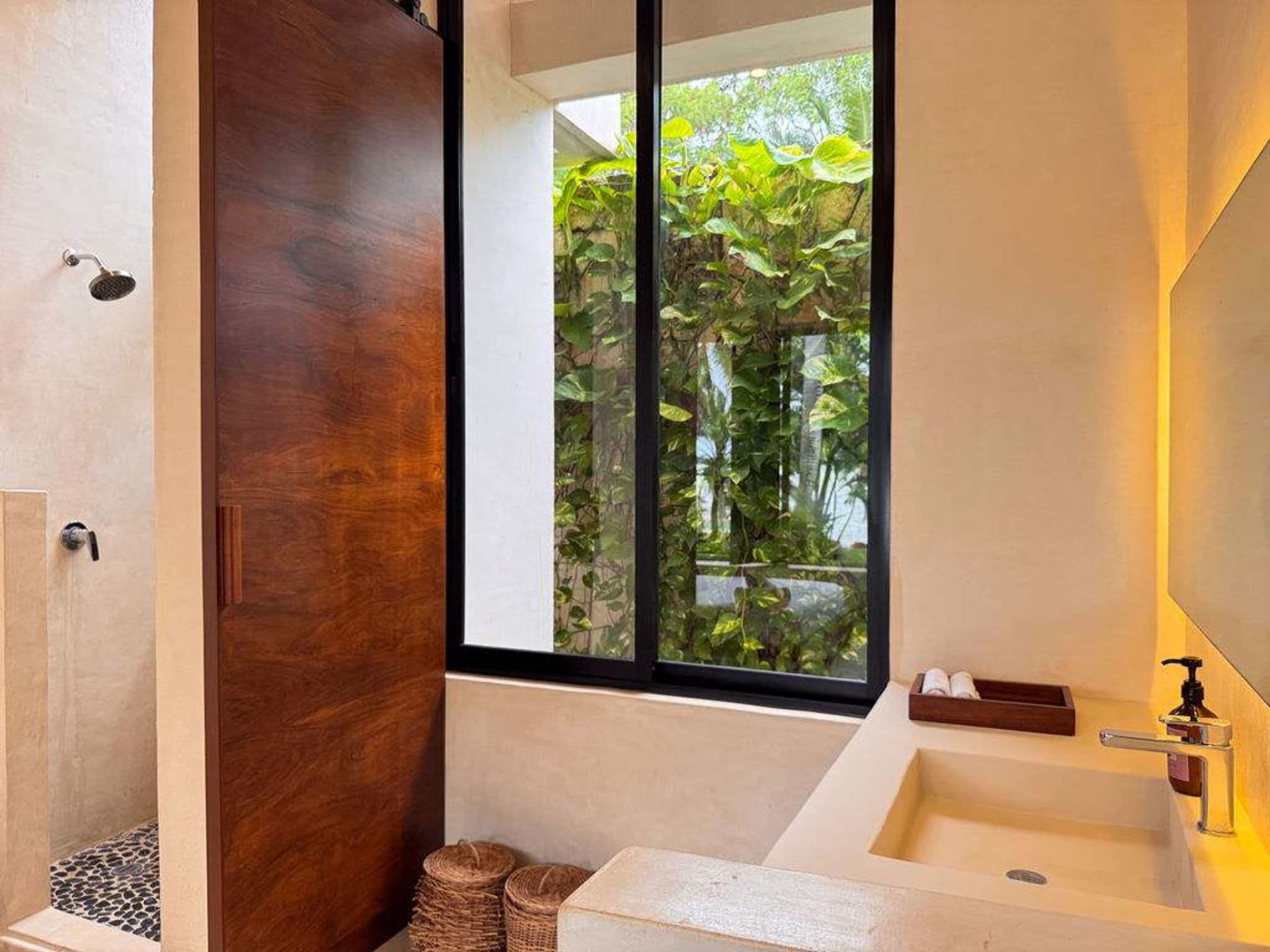 Bathroom with a sink, shower, and a wooden door overlooking a garden.