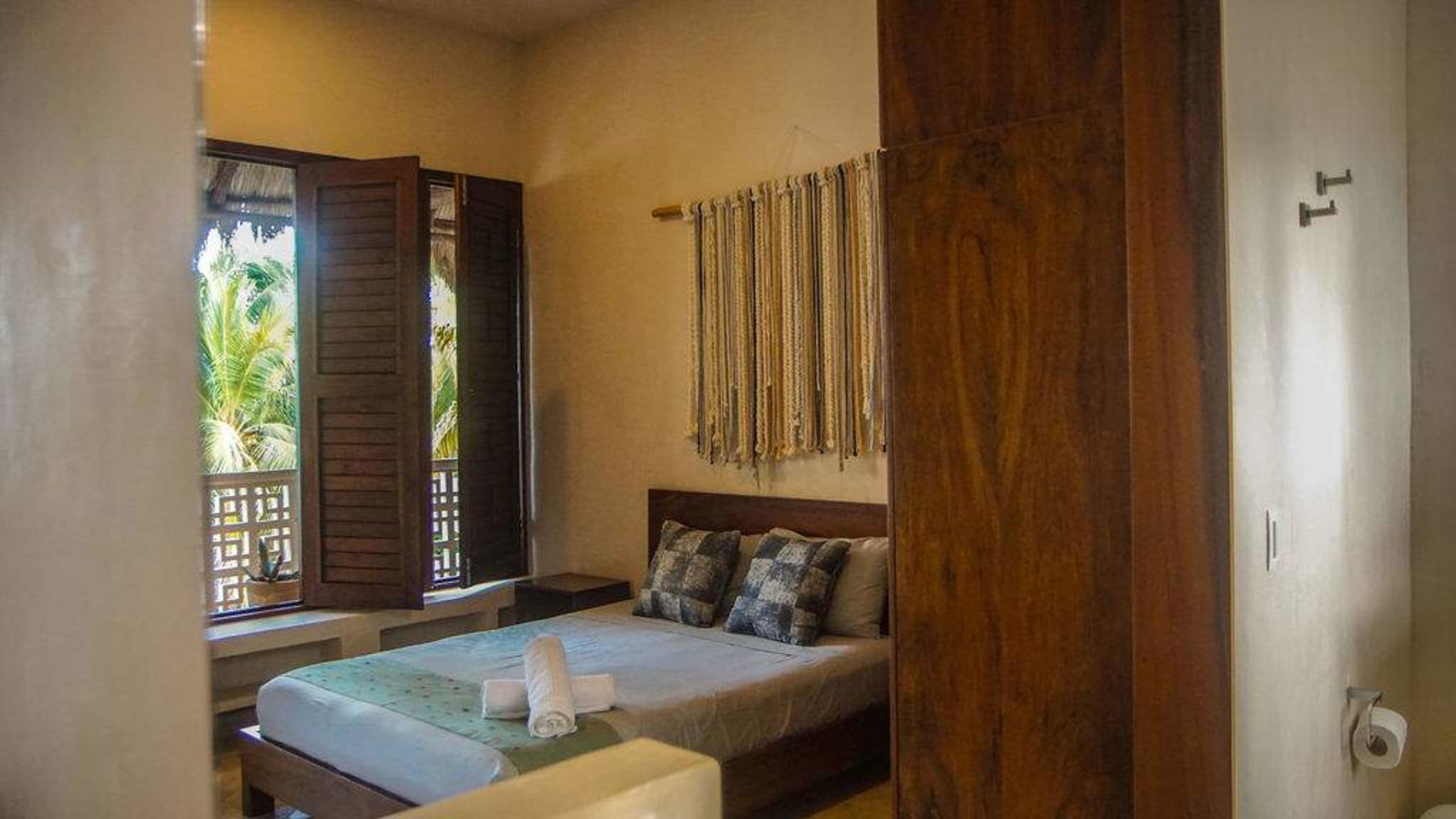 A bedroom with a bed, pillows, and a macrame wall hanging.