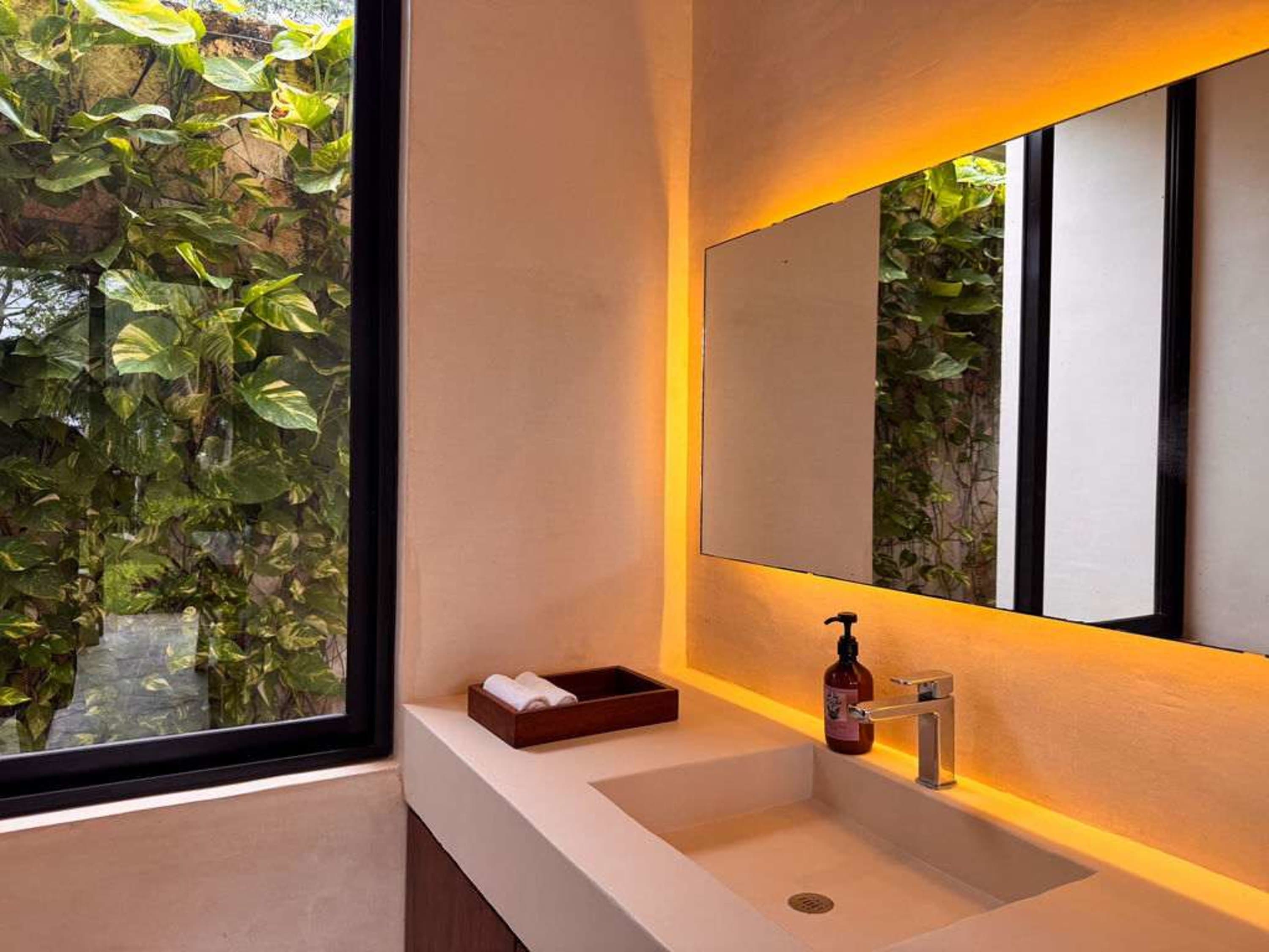 A modern bathroom with a sink, faucet, mirror, and lush greenery outside the window.