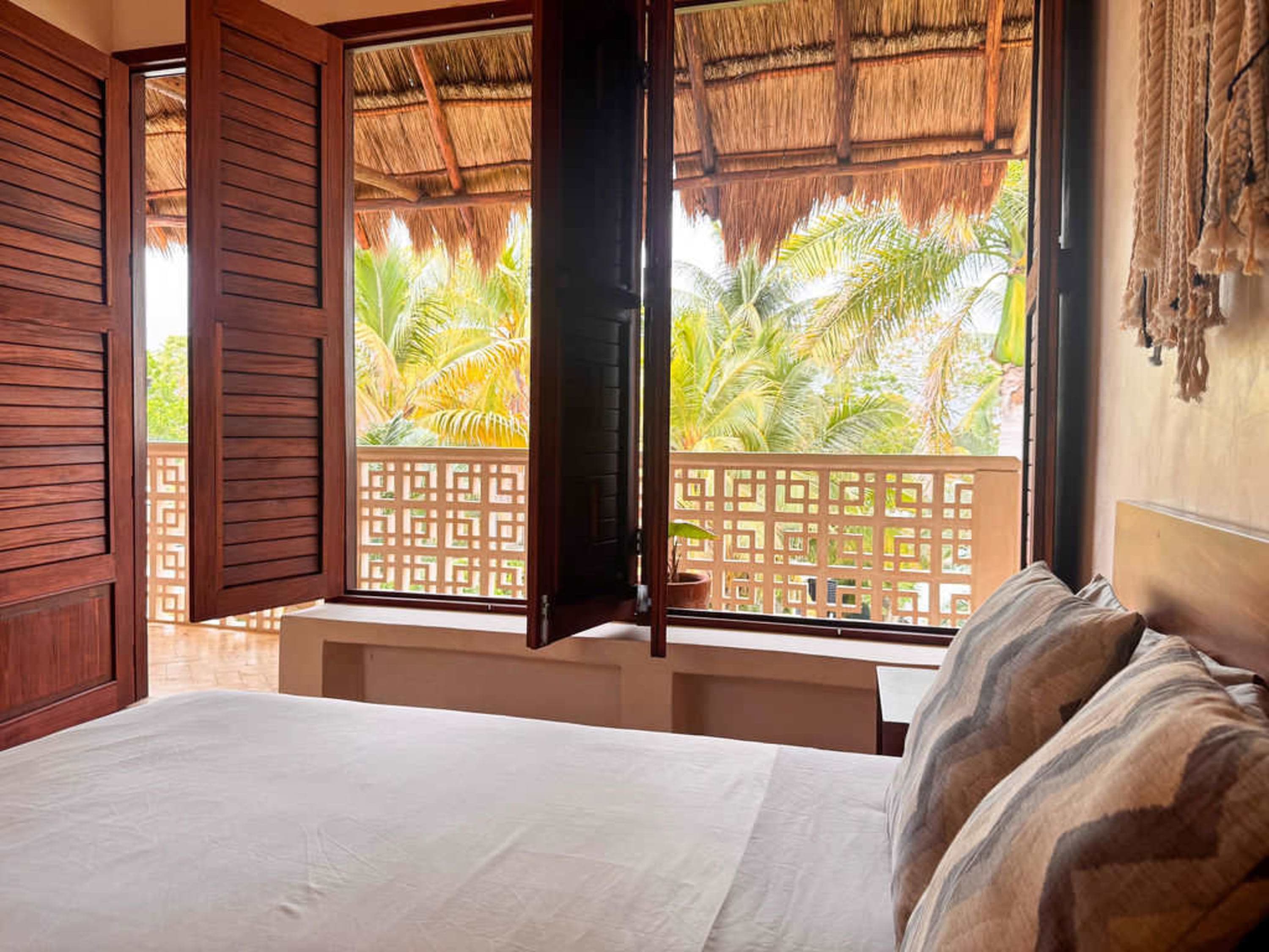 Bedroom with open wooden shutters revealing a tropical balcony view.