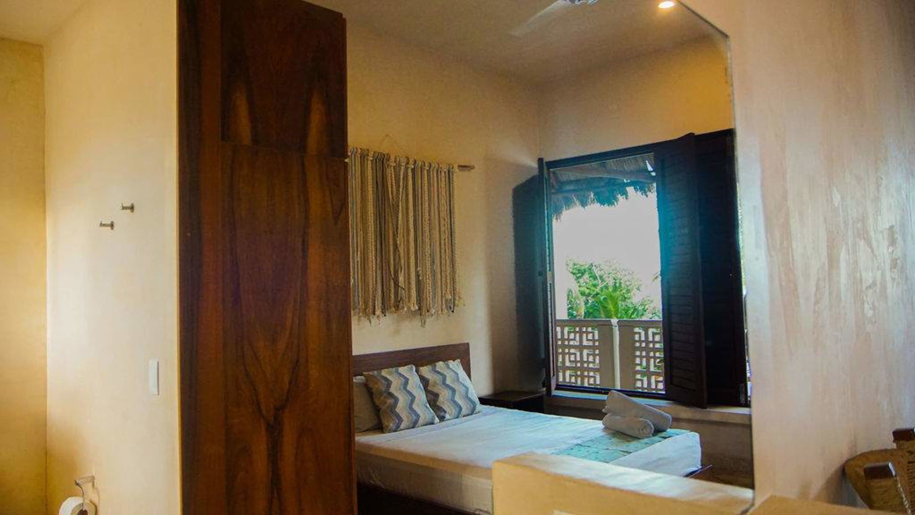 A wooden wardrobe stands next to a bed with patterned pillows and a roll of toilet paper.