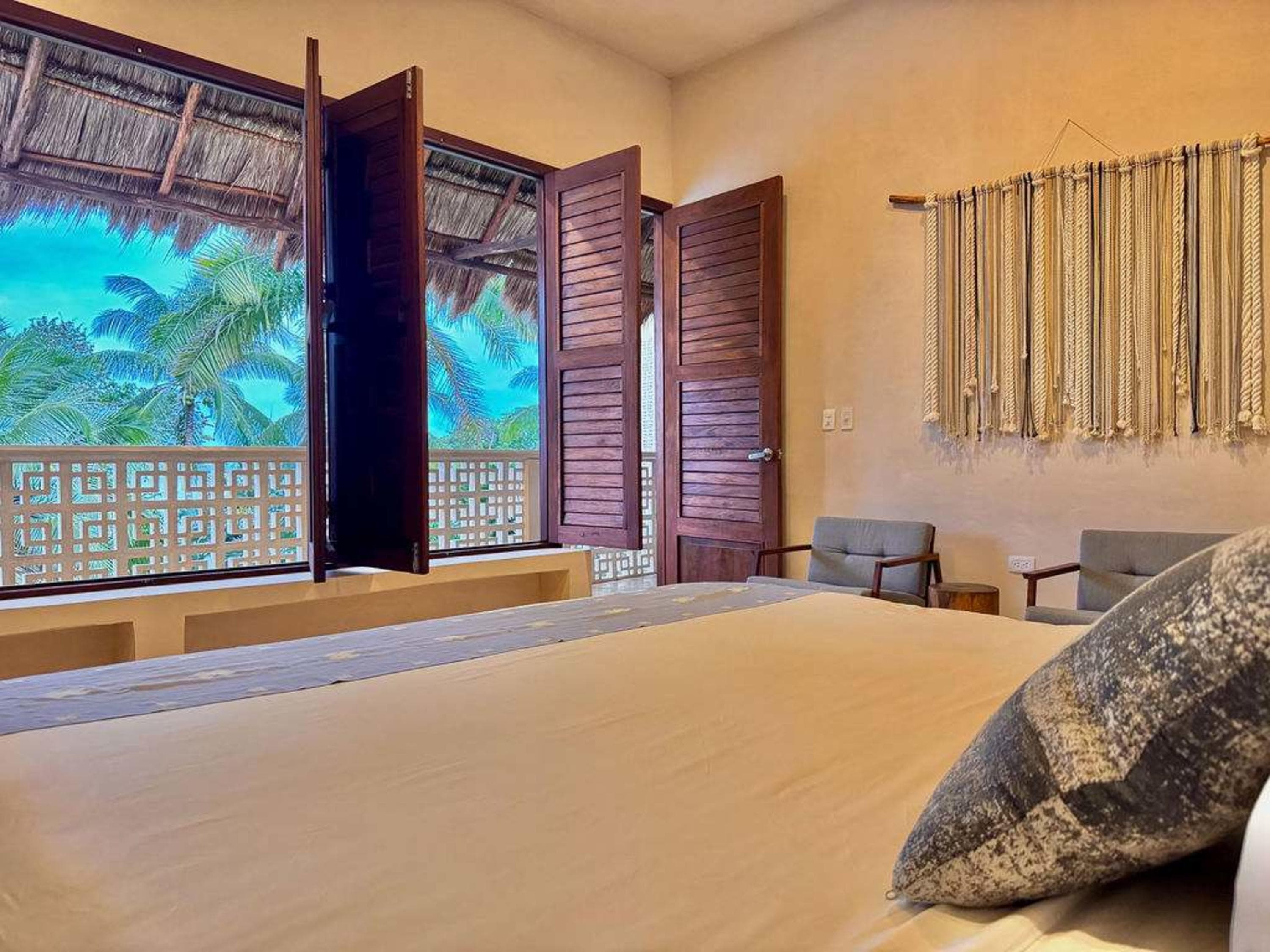A serene bedroom with a bed and a beautiful view of palm trees and the ocean through a window.