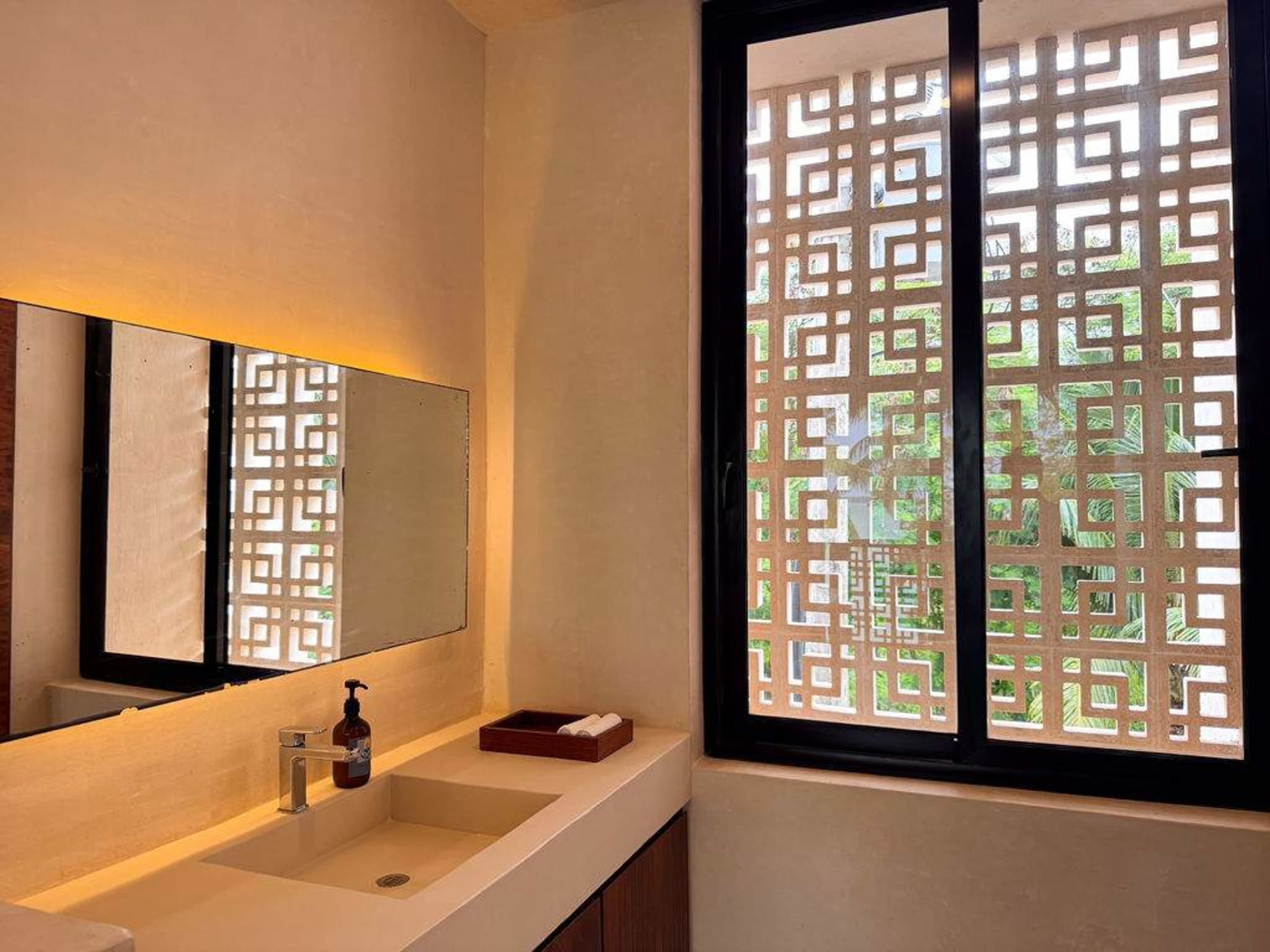 A modern bathroom with a concrete sink and countertop, a large mirror, and a decorative screen windo