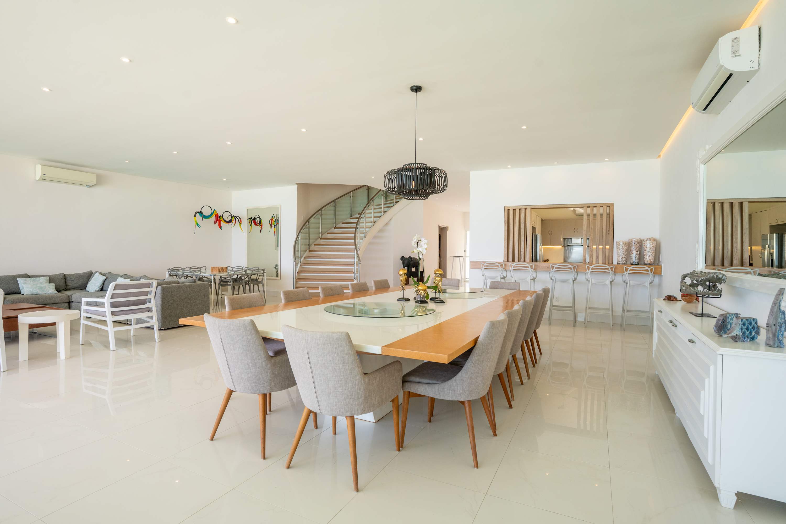 Modern dining room with large table, chairs, staircase, and bar area.