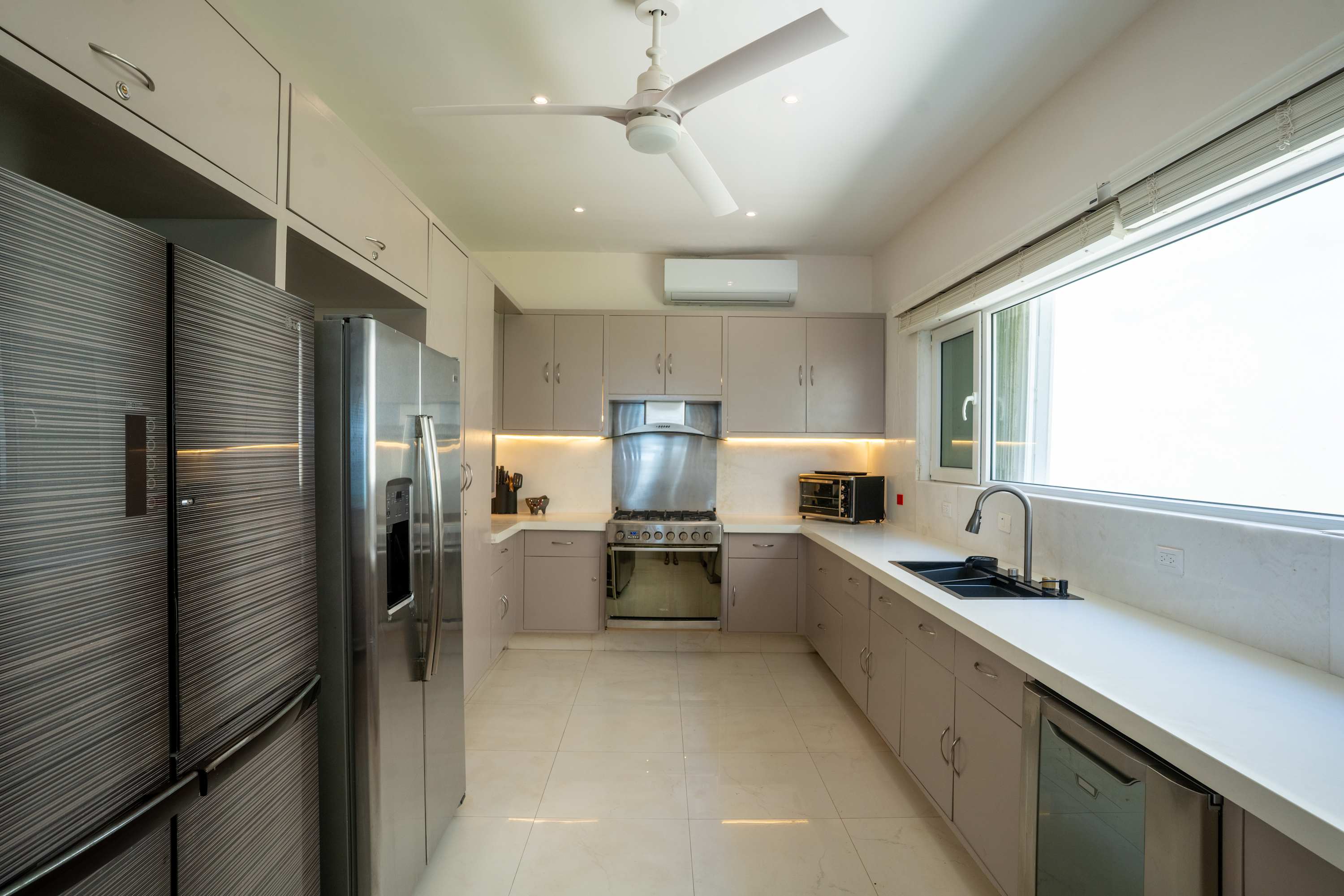 A modern kitchen with stainless steel appliances, light gray cabinets, and a large window.