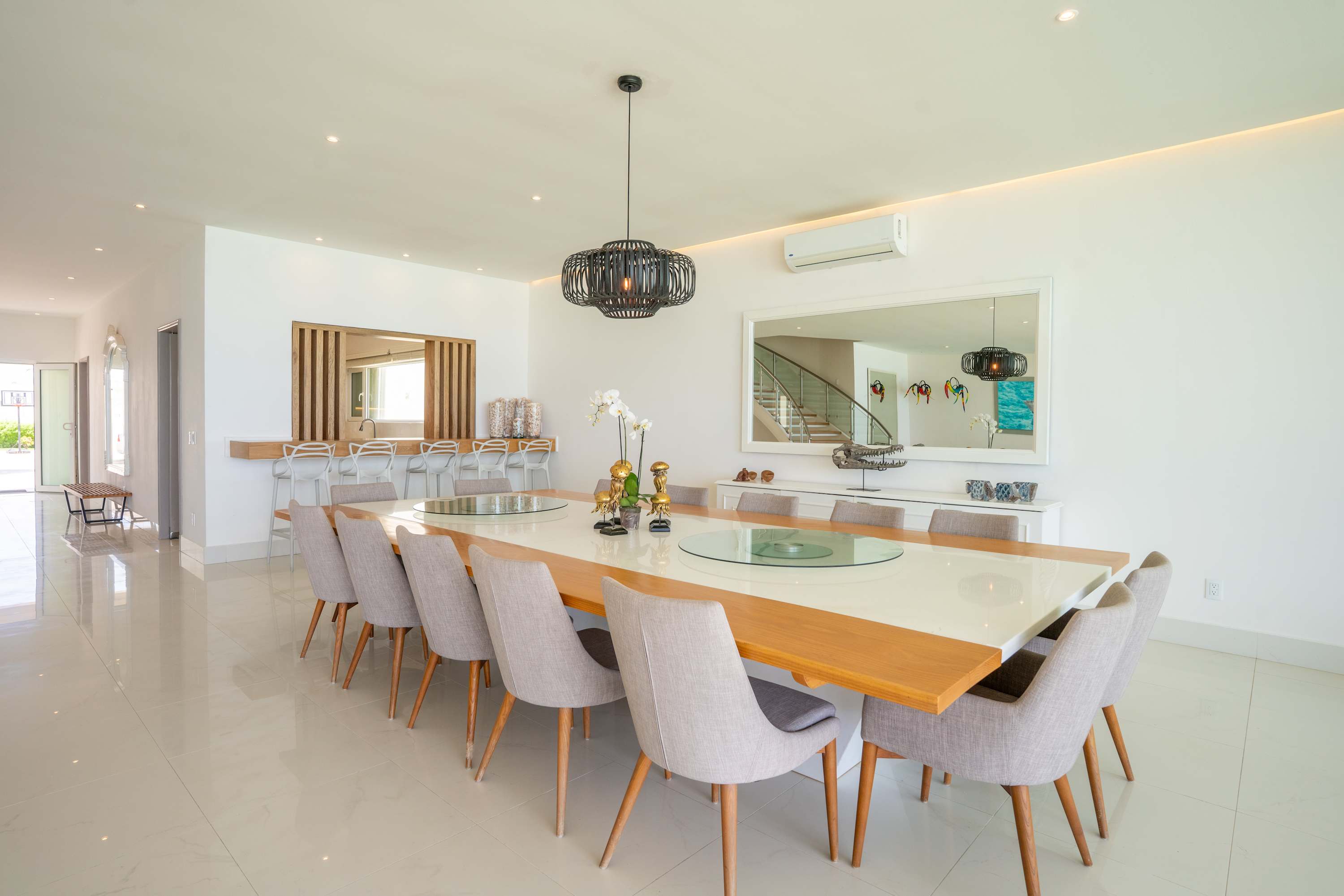 A modern dining room with a long white table and upholstered chairs.