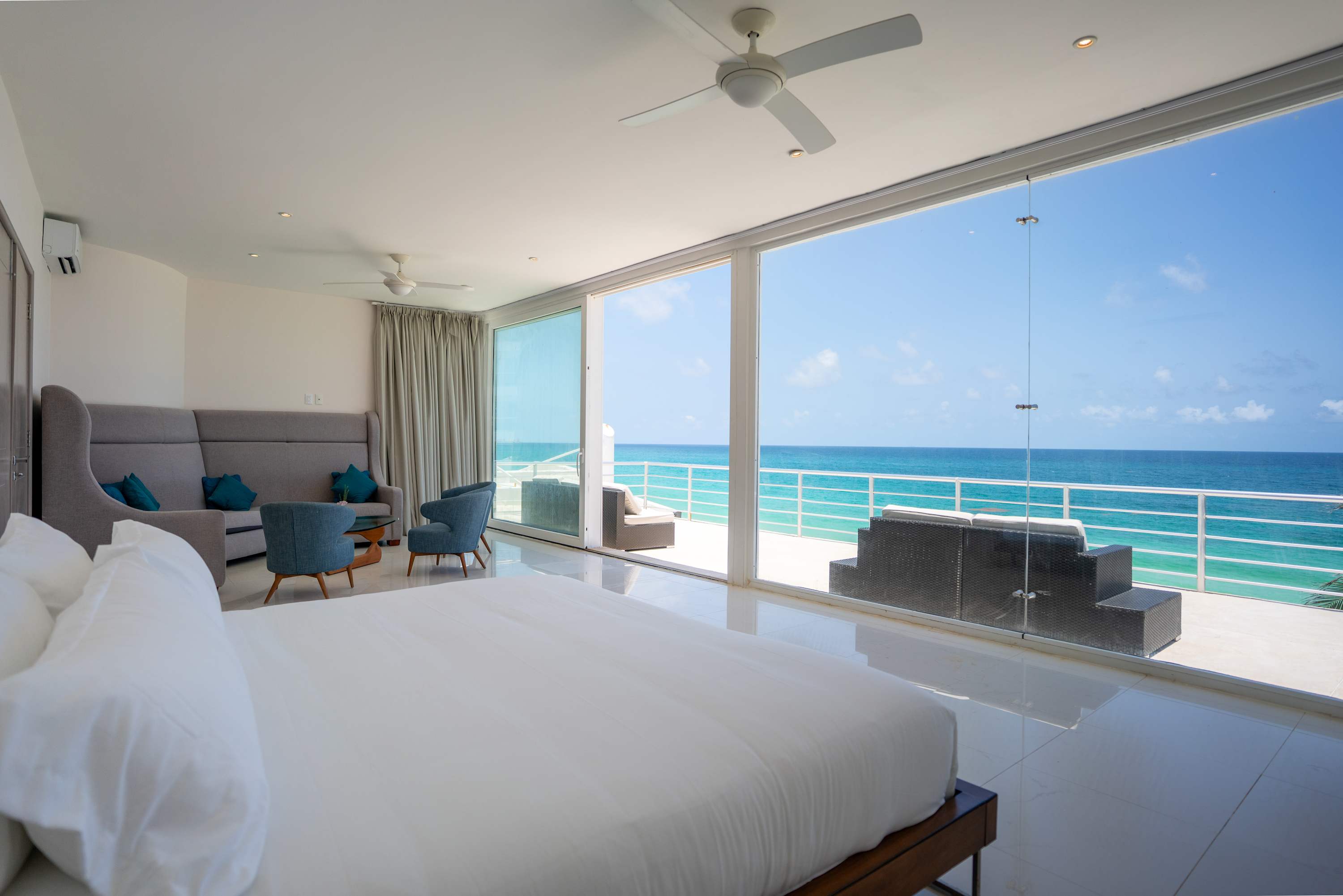 A bright bedroom with a large bed, couches, and a balcony overlooking the ocean.