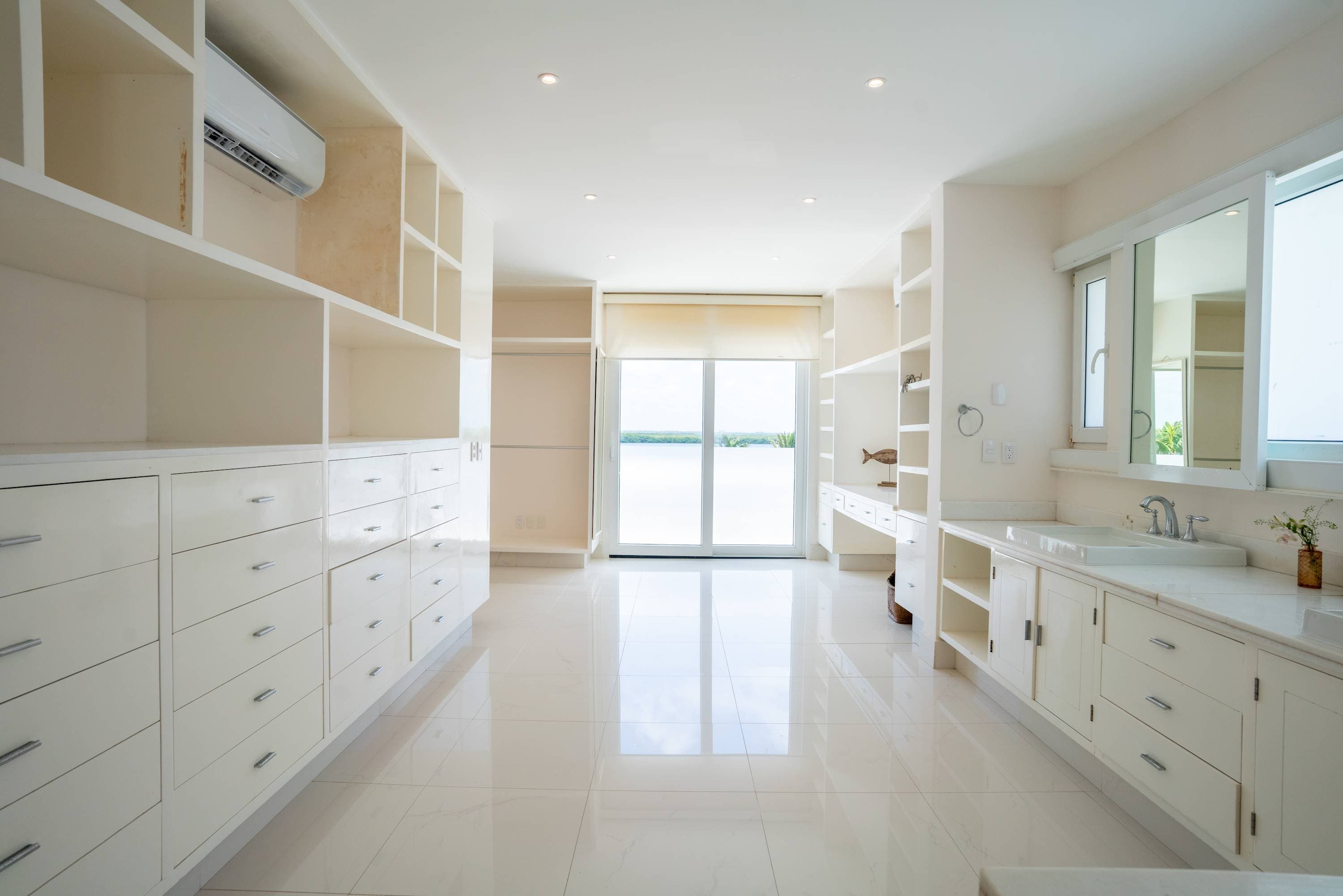 A bright, modern closet with built-in white cabinets and drawers and a view of the water.