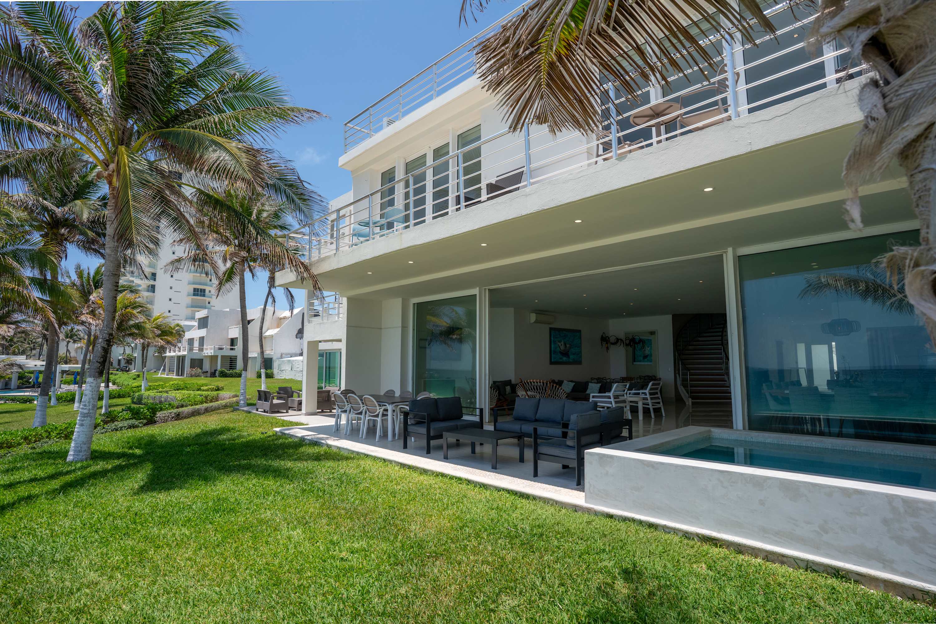 A modern, white multi-story house with balconies, palm trees, and a small pool.