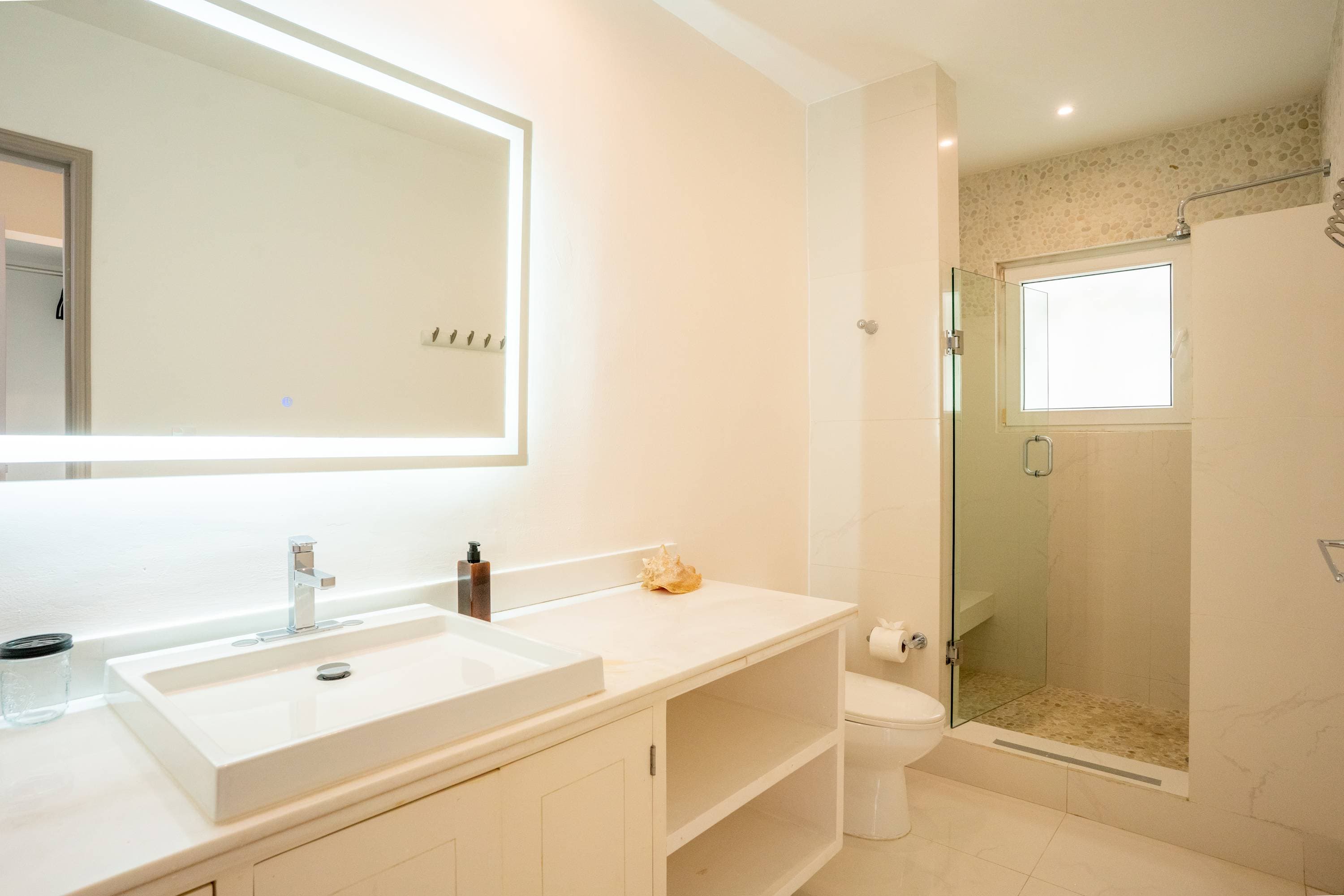 A modern bathroom with a large mirror, vessel sink, toilet, and walk-in shower.