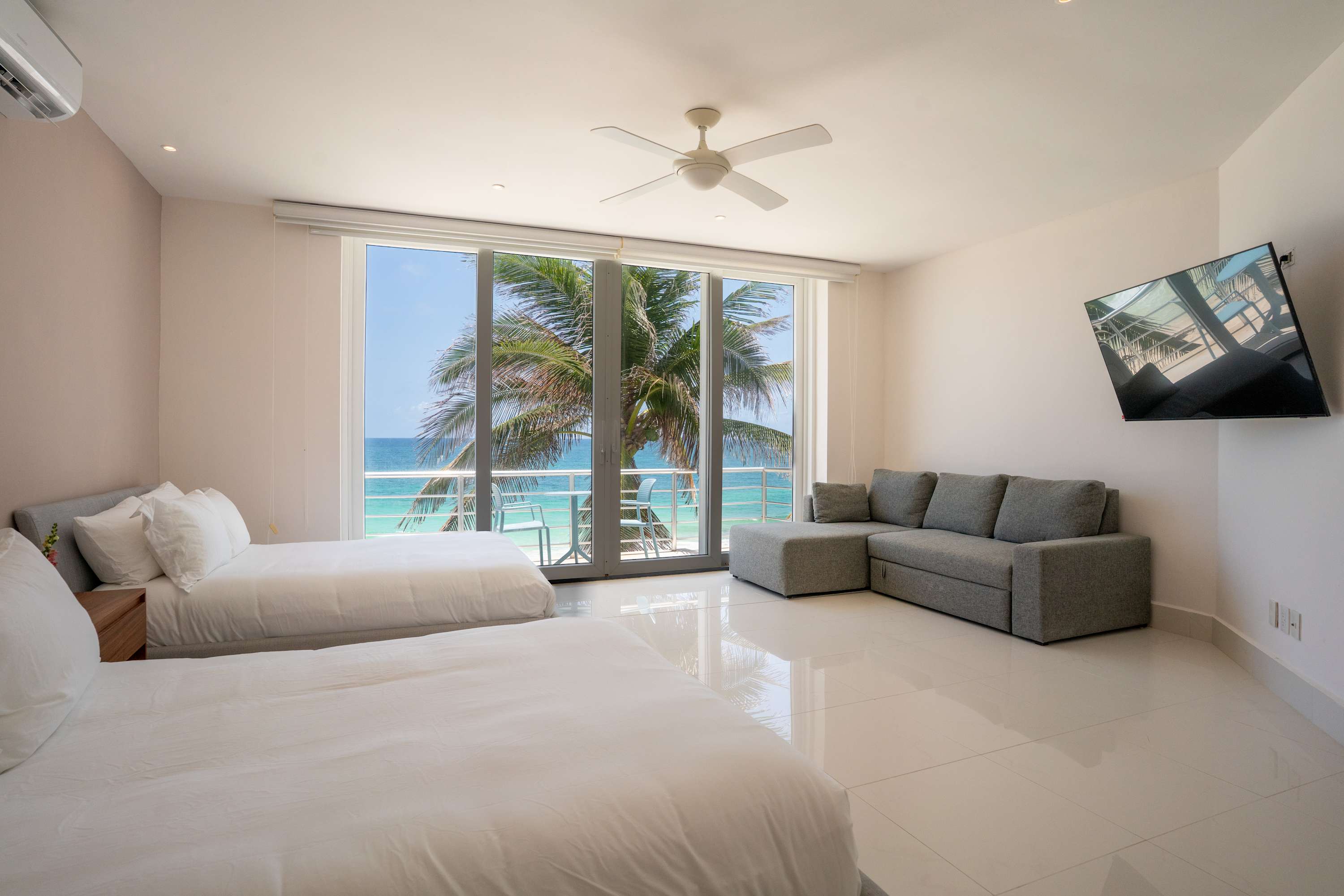 A bright bedroom with two beds and a view of the ocean.