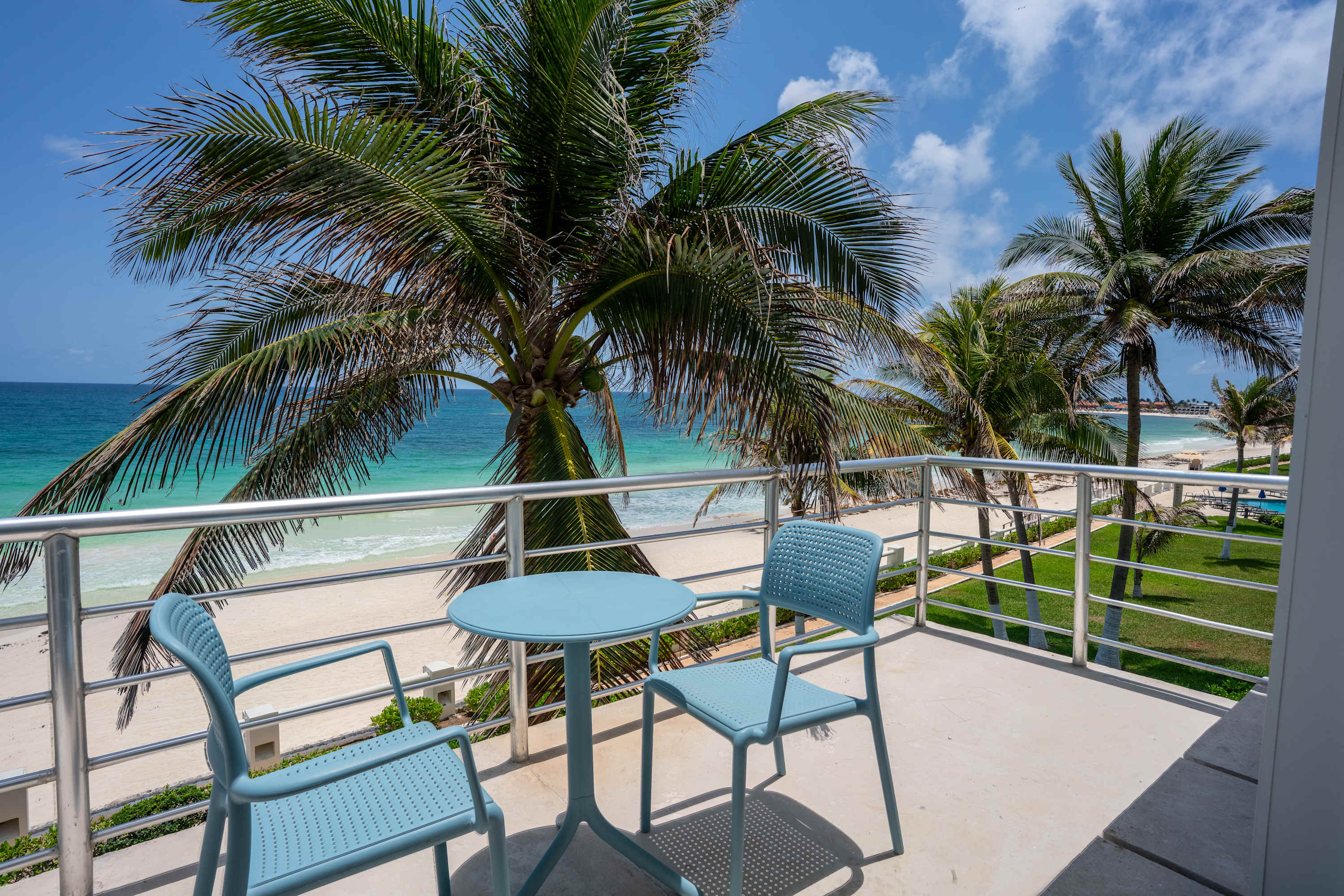 Balcony with chairs and table overlooking a tropical beach with palm trees.